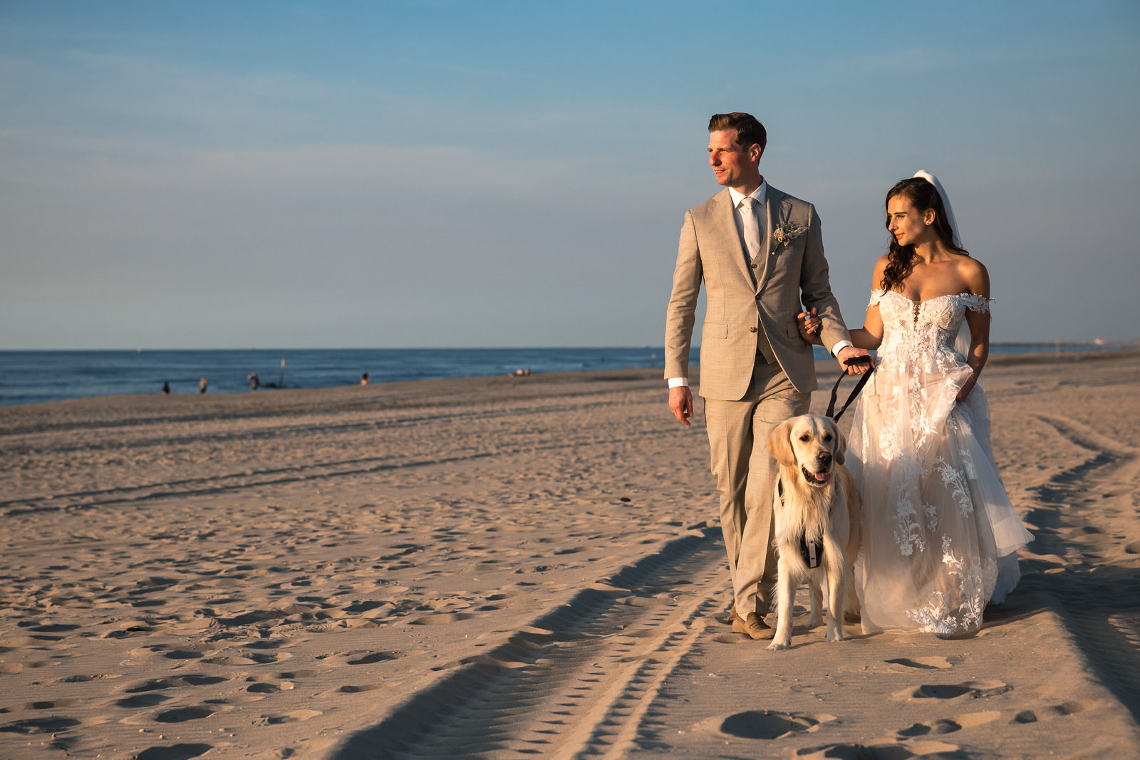 Bride groom and dog walking down the beach during sunset