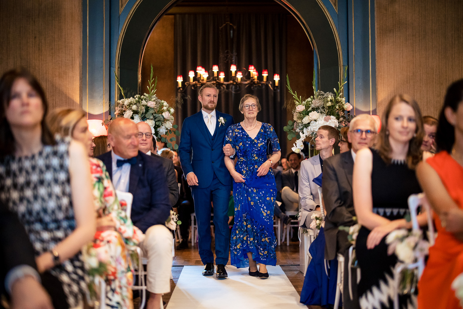 Bruidegom en moeder lopen samen naar voren voor de trouwceremonie door trouwfotograaf Den Haag