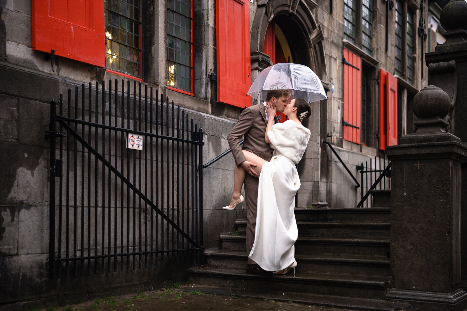 Bruidspaar kussend op de trap terwijl bruid haar been opgetilt wordt en zichtbaar is in haar split van de jurk vastgelegd door Trouwfotograaf Den Haag Paco van Leeuwen