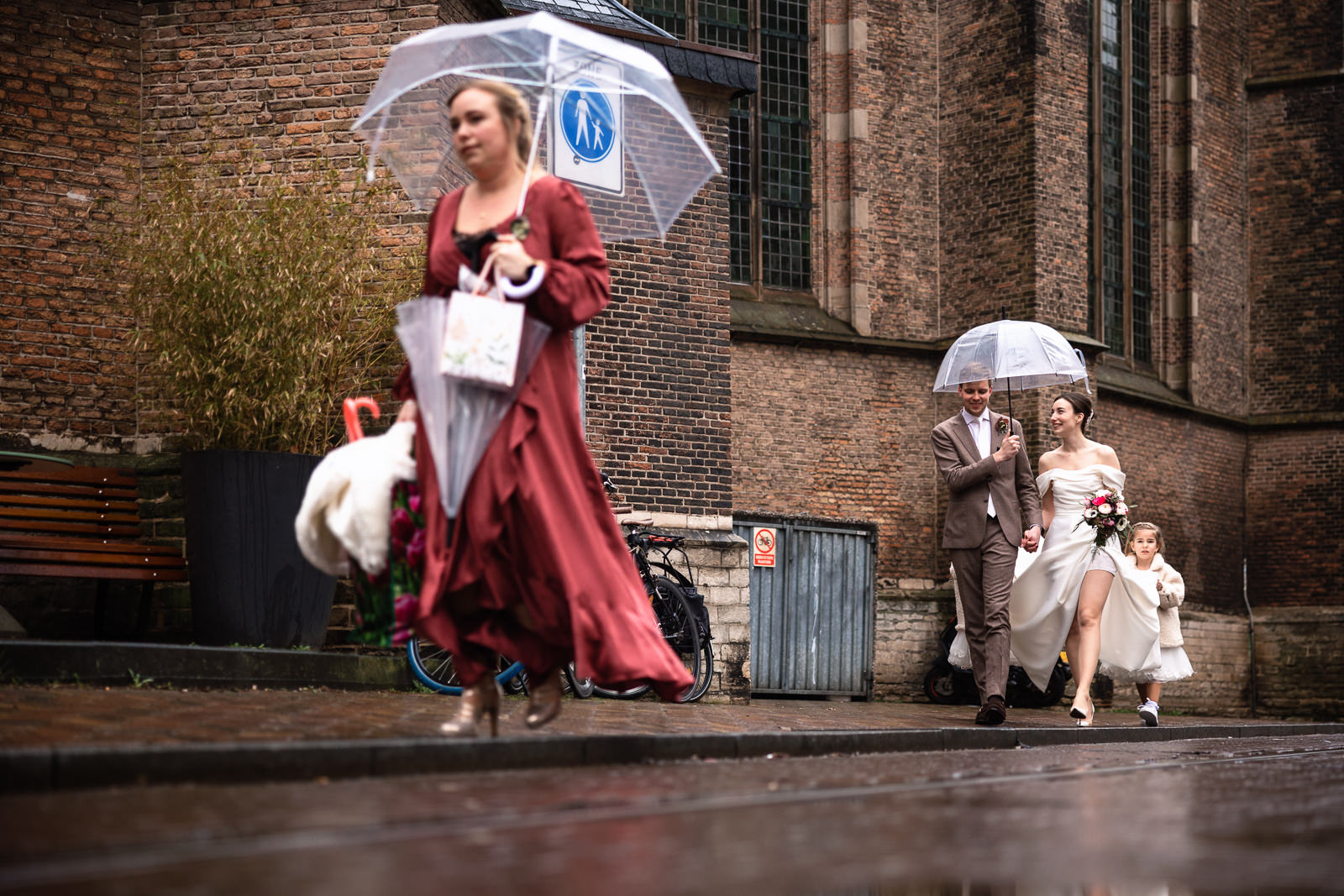 Bruidspaar loopt door de regen van oude stadhuis naar het nutshuis voor receptie
