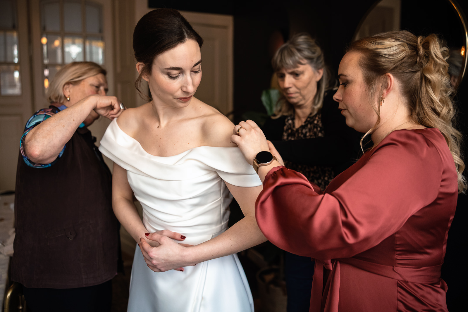 Moeder, schoonmoeder en vriendin helpen de bruid met de laatste details van de jurk aandoen vastgelegd door Trouwfotograaf Den Haag Paco van Leeuwen