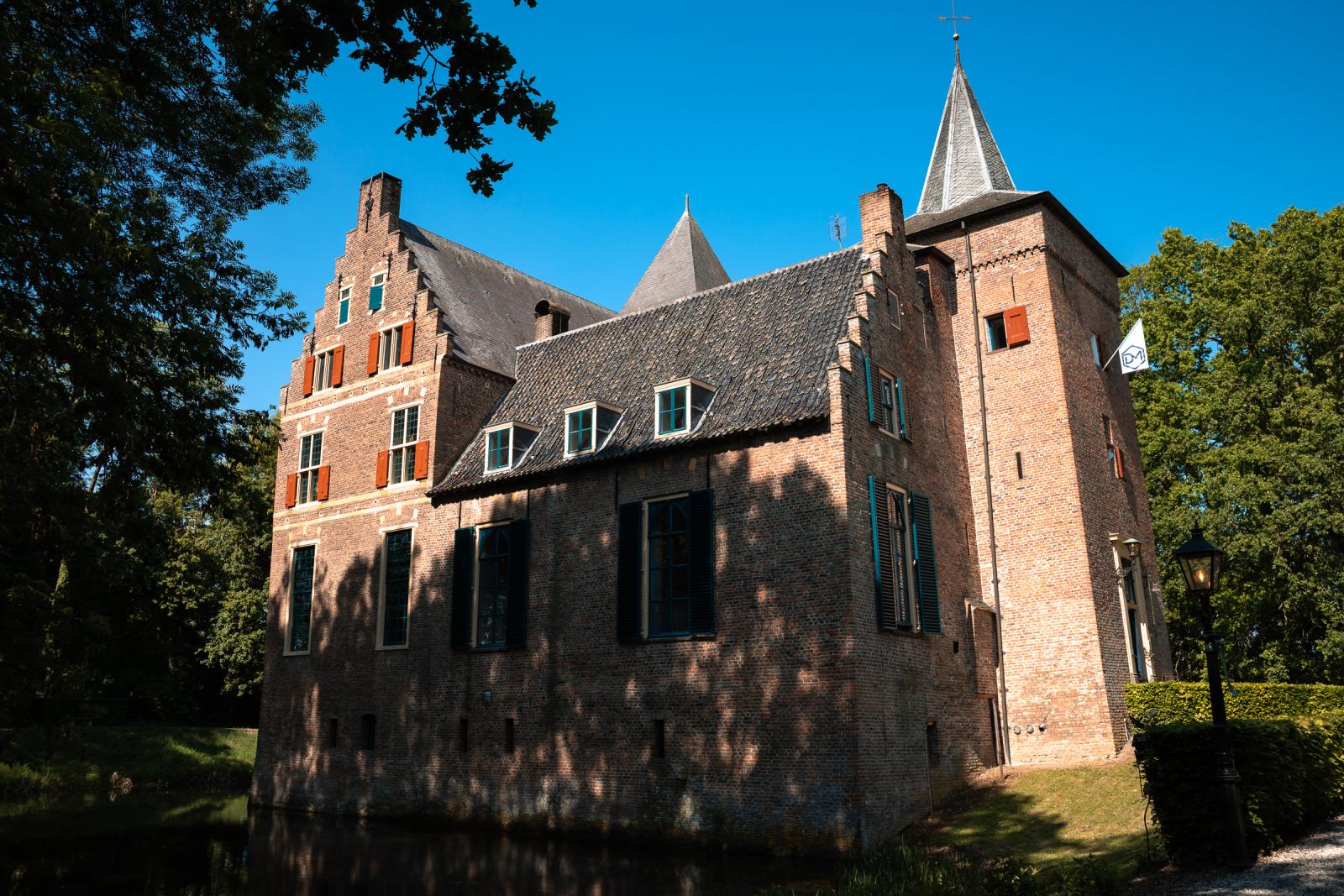 Zijaanzicht van de historische, bakstenen gevel en de toren van Kasteel Wijenburg in Echteld onder een strakblauwe lucht