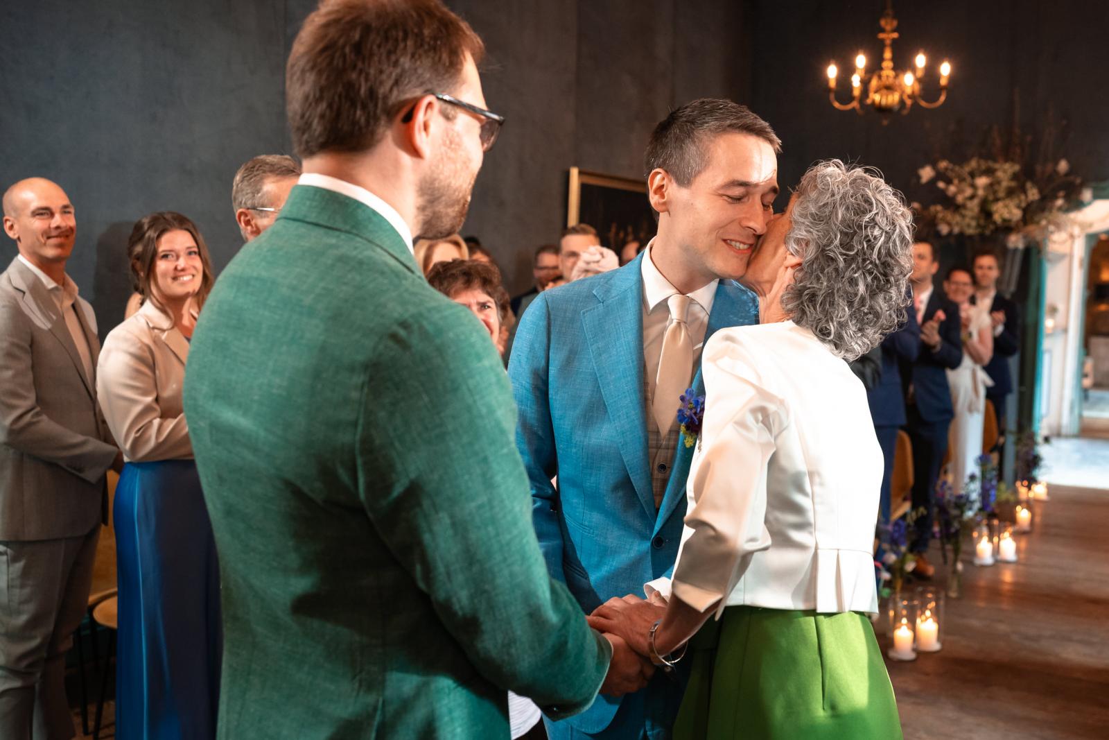 Daan kust zijn emotionele moeder op haar wang bij het altaar, terwijl Martijn glimlachend toekijkt te midden van de daggasten