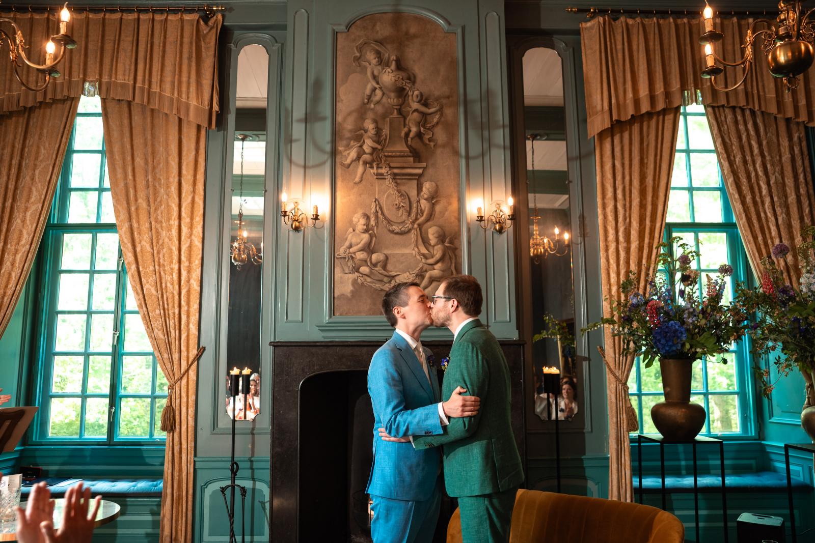 Daan en Martijn bezegelen hun huwelijk met een intieme kus voor de monumentale schouw in de klassiek ingerichte blauwe salon