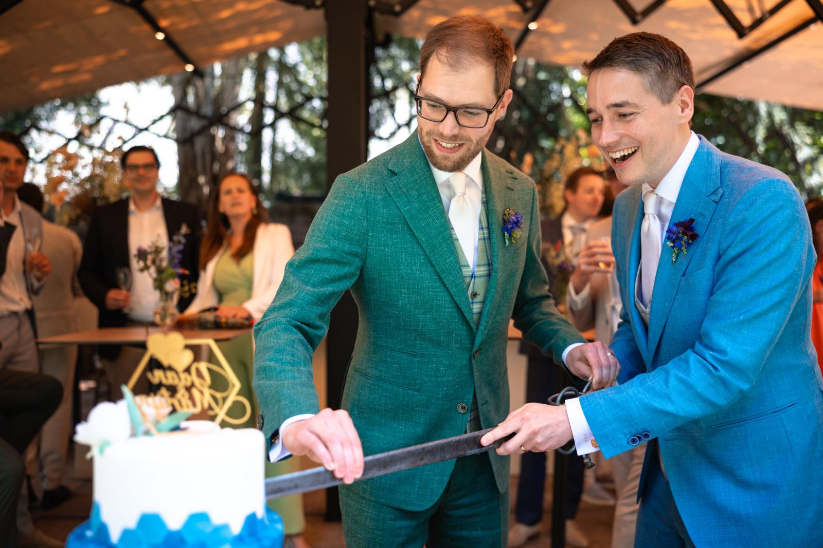 Het pasgetrouwde koppel snijdt lachend de gelaagde, blauw-witte bruidstaart aan met een groot zwaard tijdens de receptie buiten
