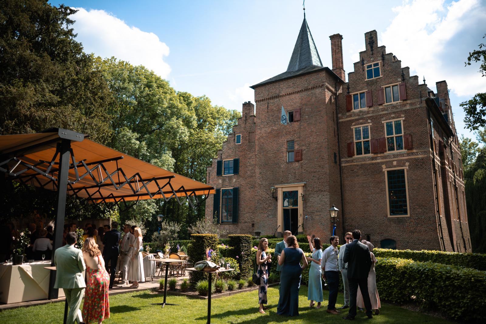 Daggasten borrelen op het zonnige gazon naast een grote stretchtent met op de achtergrond de imposante bakstenen toren van Kasteel Wijenburg