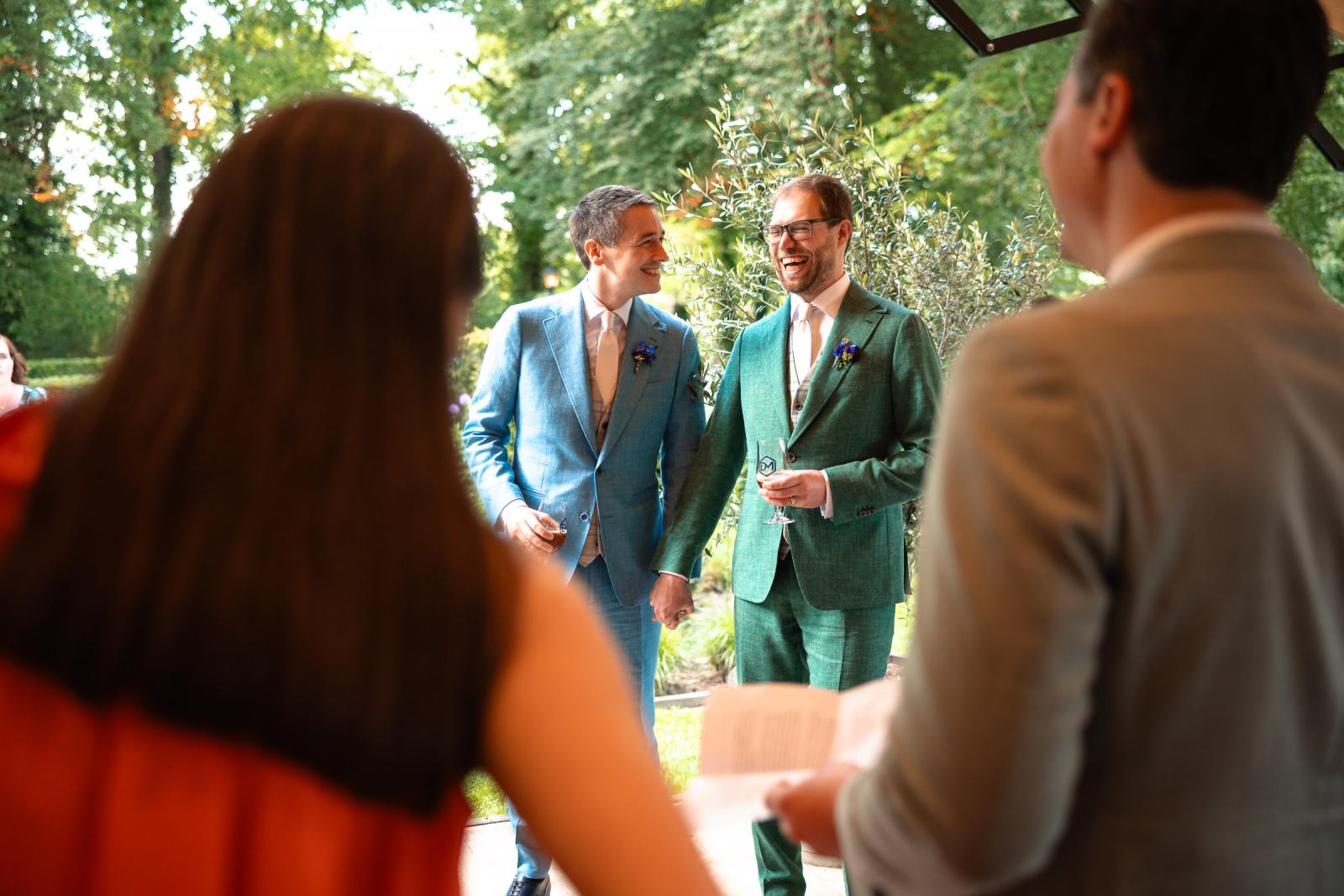 Daan en Martijn houden elkaars hand vast en lachen hartelijk tijdens een informele speech in de kasteeltuin