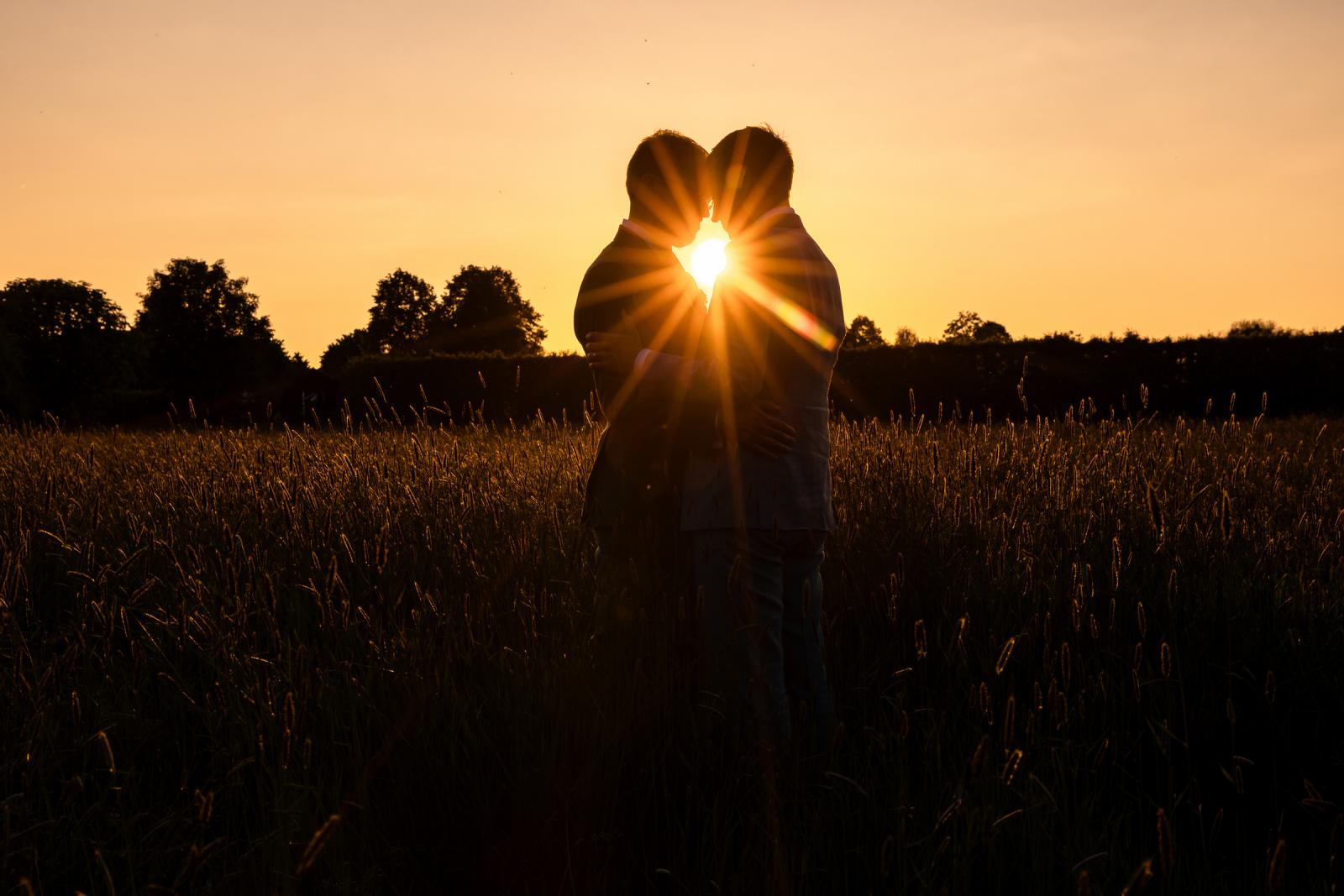 Silhouet van Daan en Martijn die elkaar omhelzen in het veld, waarbij de ondergaande zon precies tussen hen in als een felle ster doorbreekt
