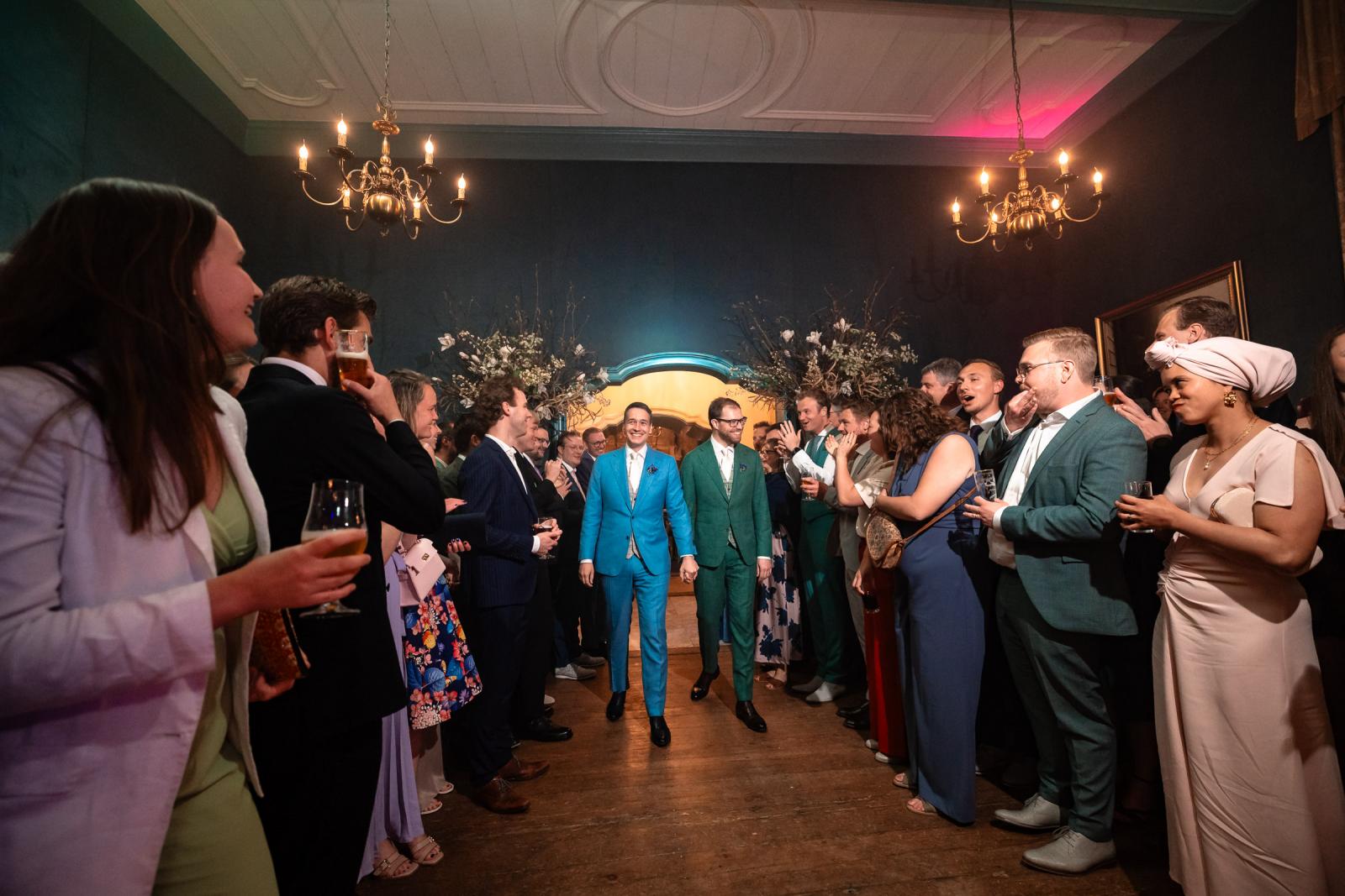 Daan en Martijn lopen hand in hand een volle zaal binnen onder luid applaus van de daggasten, klaar voor het avondfeest