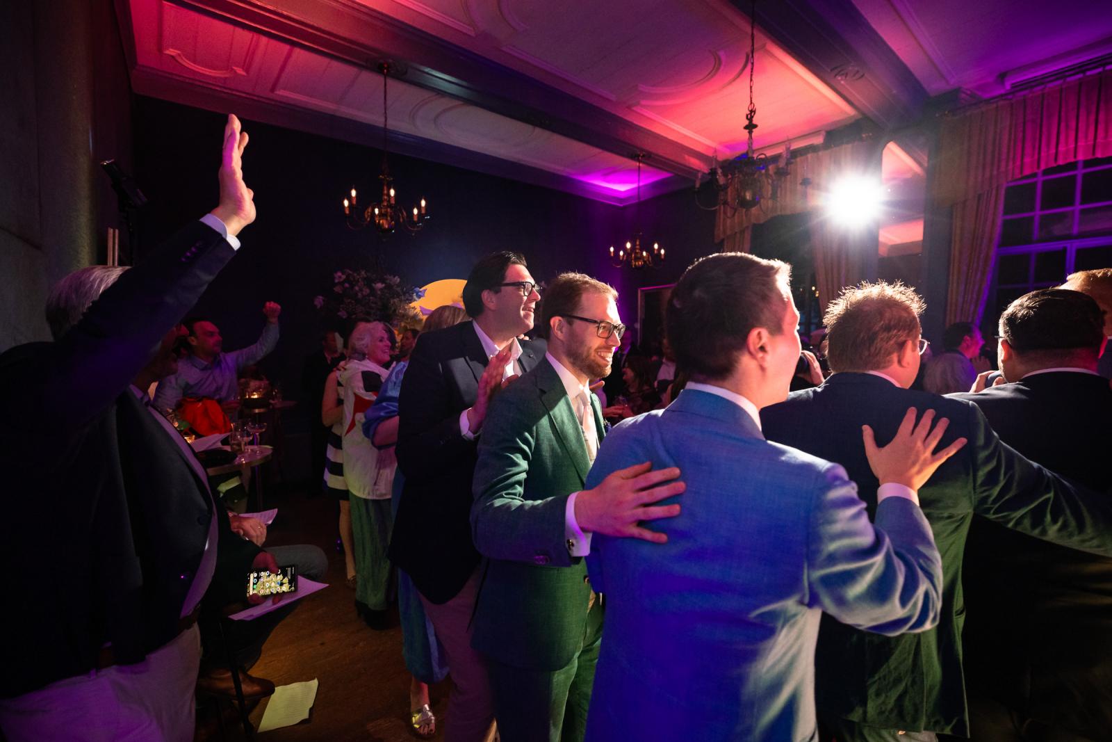 Daan en Martijn feesten mee in een polonaise tussen de daggasten in de sfeervol paars en roze verlichte ridderzaal