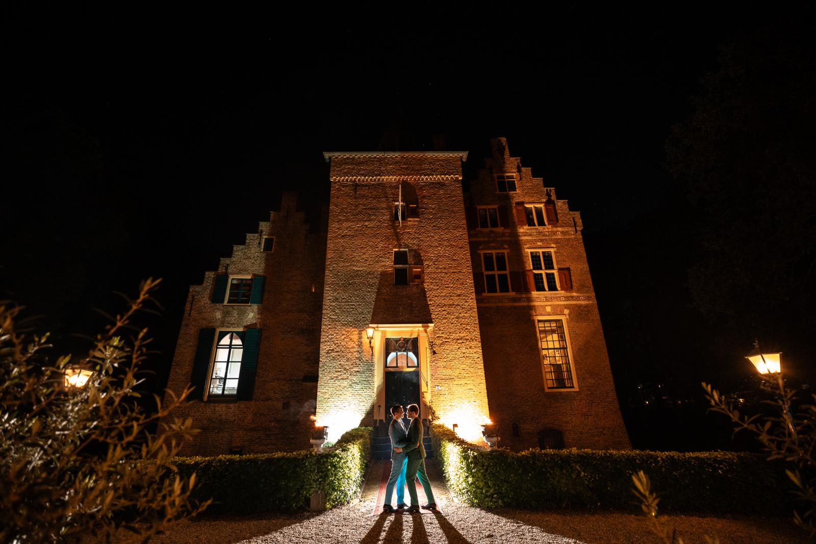 Prachtig avondportret van Kasteel Wijenburg dat volledig is uitgelicht, met Daan en Martijn die elkaar omhelzen op het verlichte toegangspad