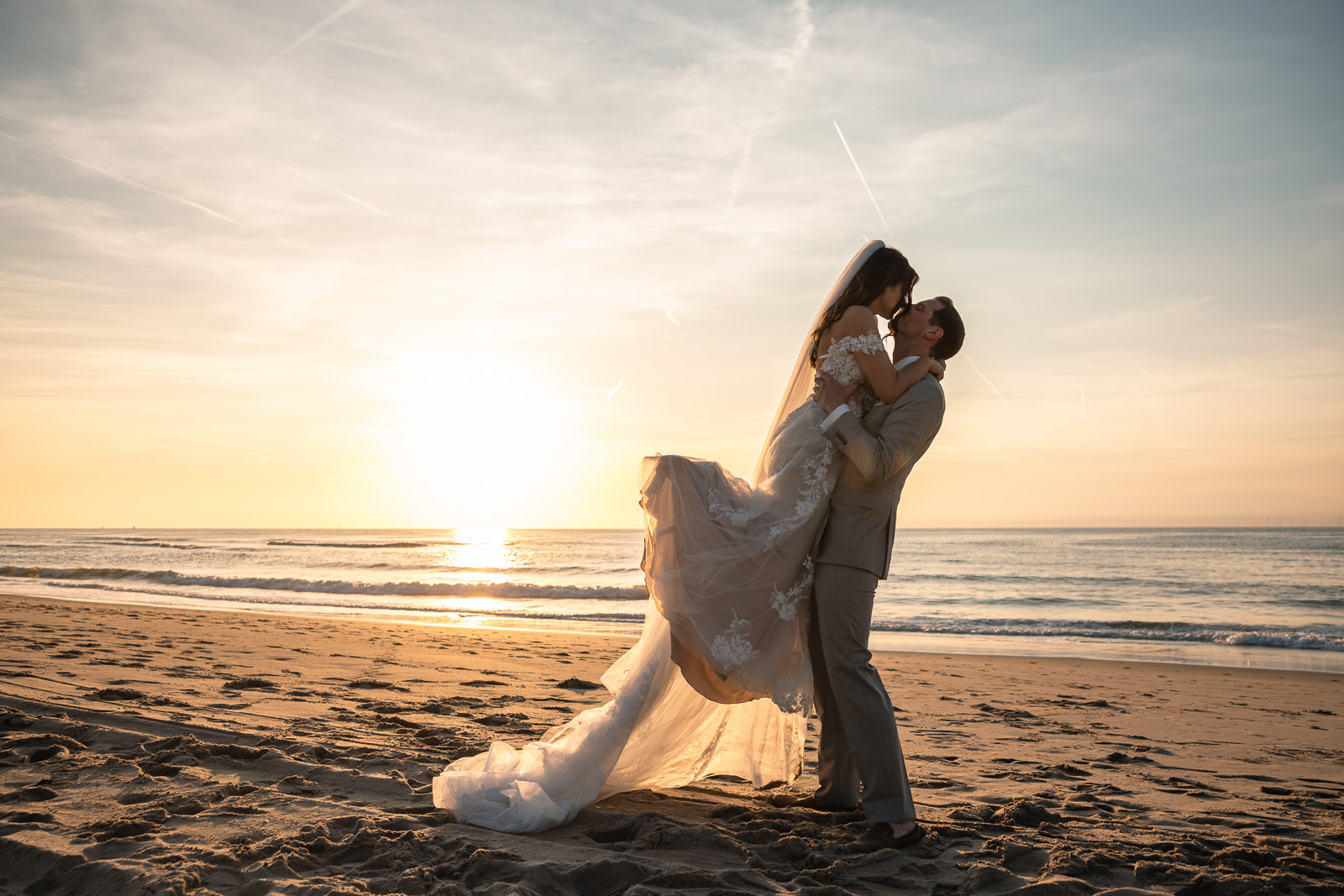 Groom picks his bride up and kisses her during sunset