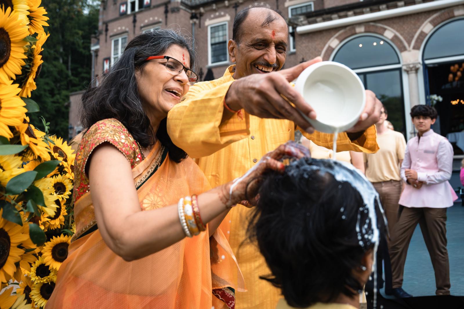 Ouders bruidegom doen yoghurt over de bruidegom tijdens Indiase Haldi ceremonie op terras van Landgoed Duin en Kruidberg