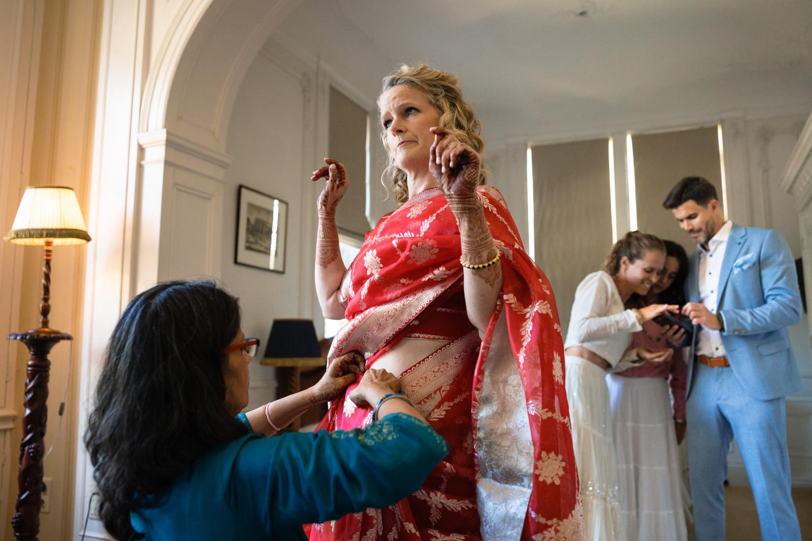 Schoonmoeder helpt bruid Anouck met aankleden in traditionele Indiase trouwkleding