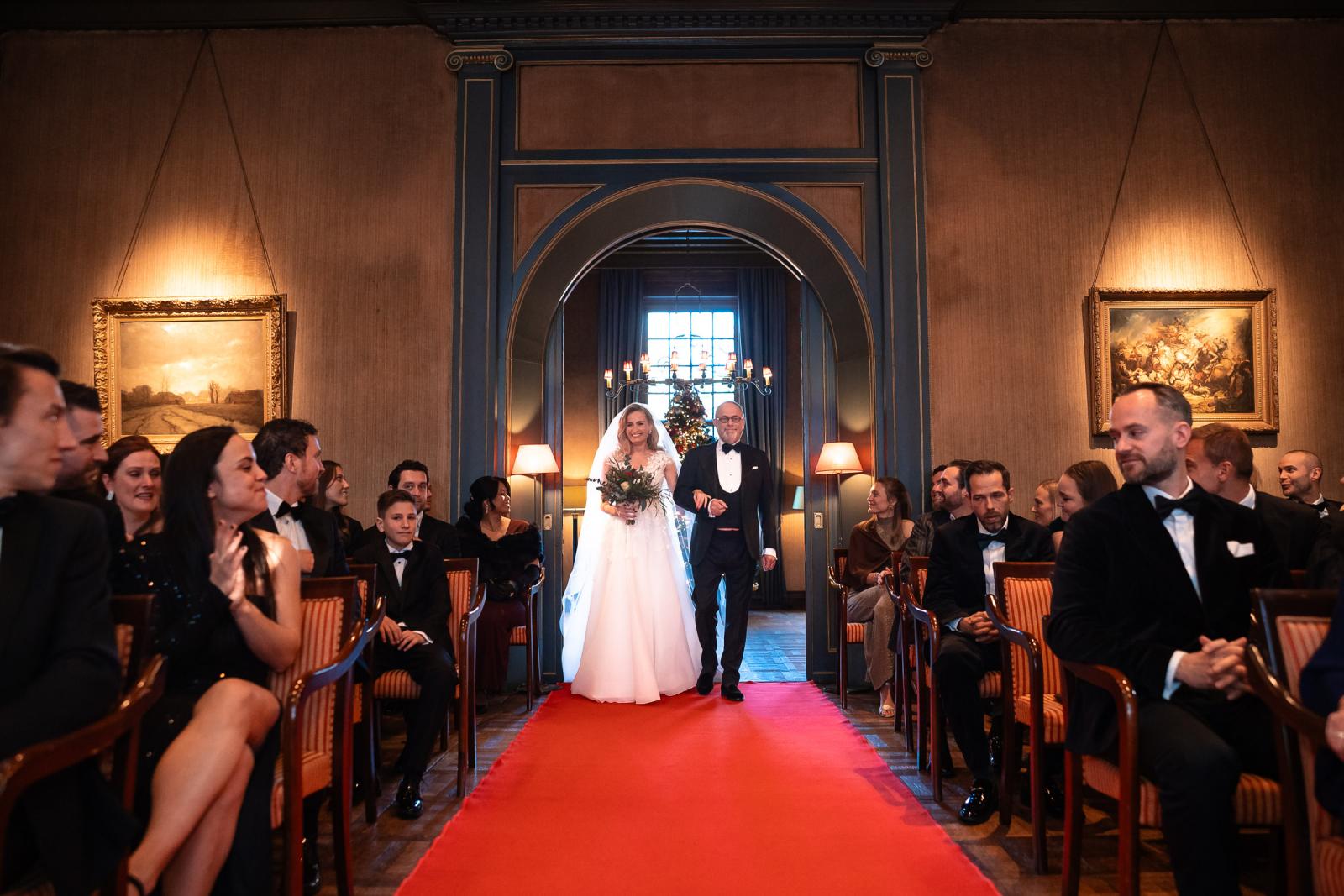 Bruid loopt met haar vader de rode loper op tijdens de kerstceremonie.