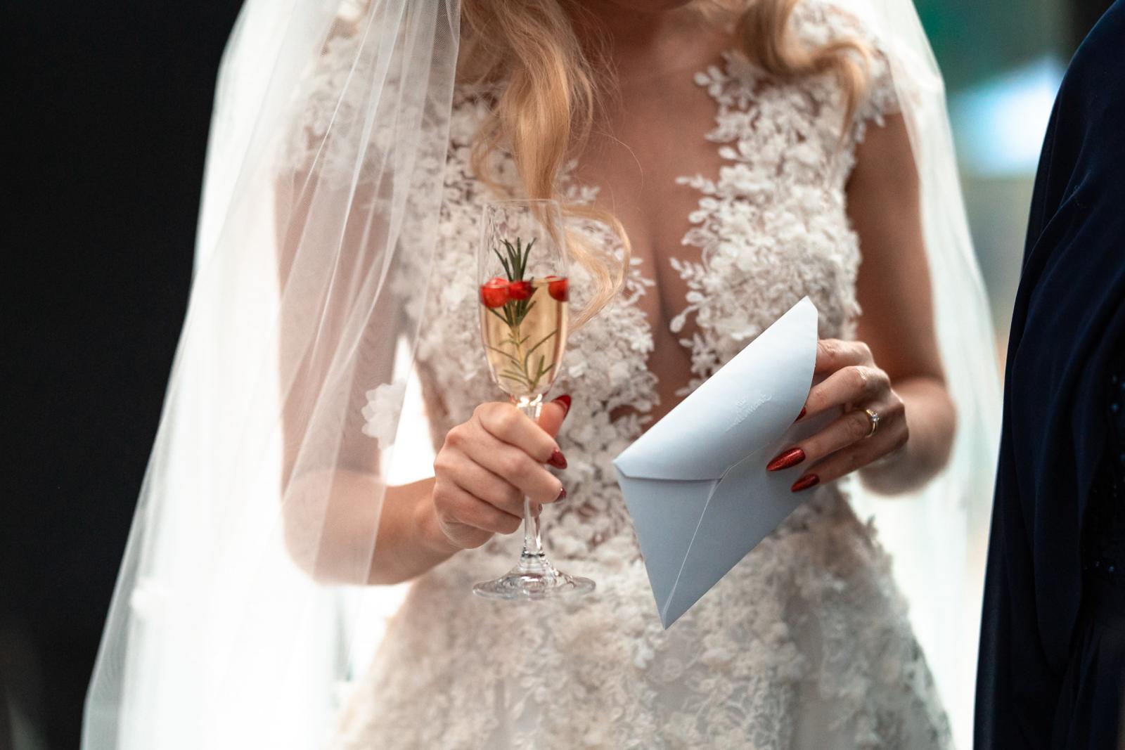 Close-up van bruidsjurk, glas champagne met rode besjes en envelop.