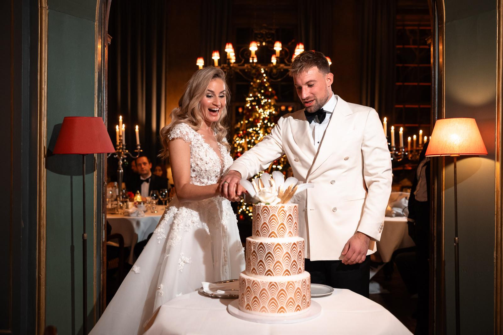 Bruidspaar snijdt de Art Deco bruidstaart aan bij kerstboom.