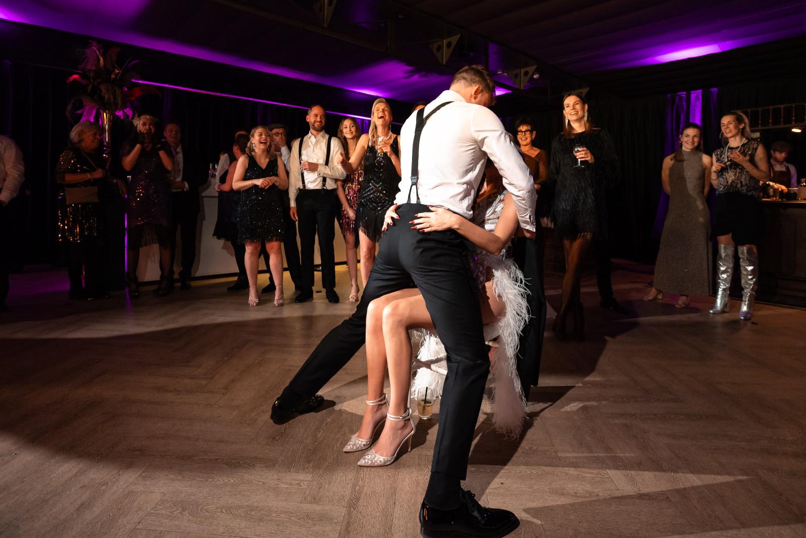 Bruidegom verrast bruid met een eigen dansact, gasten lachen en juichen.