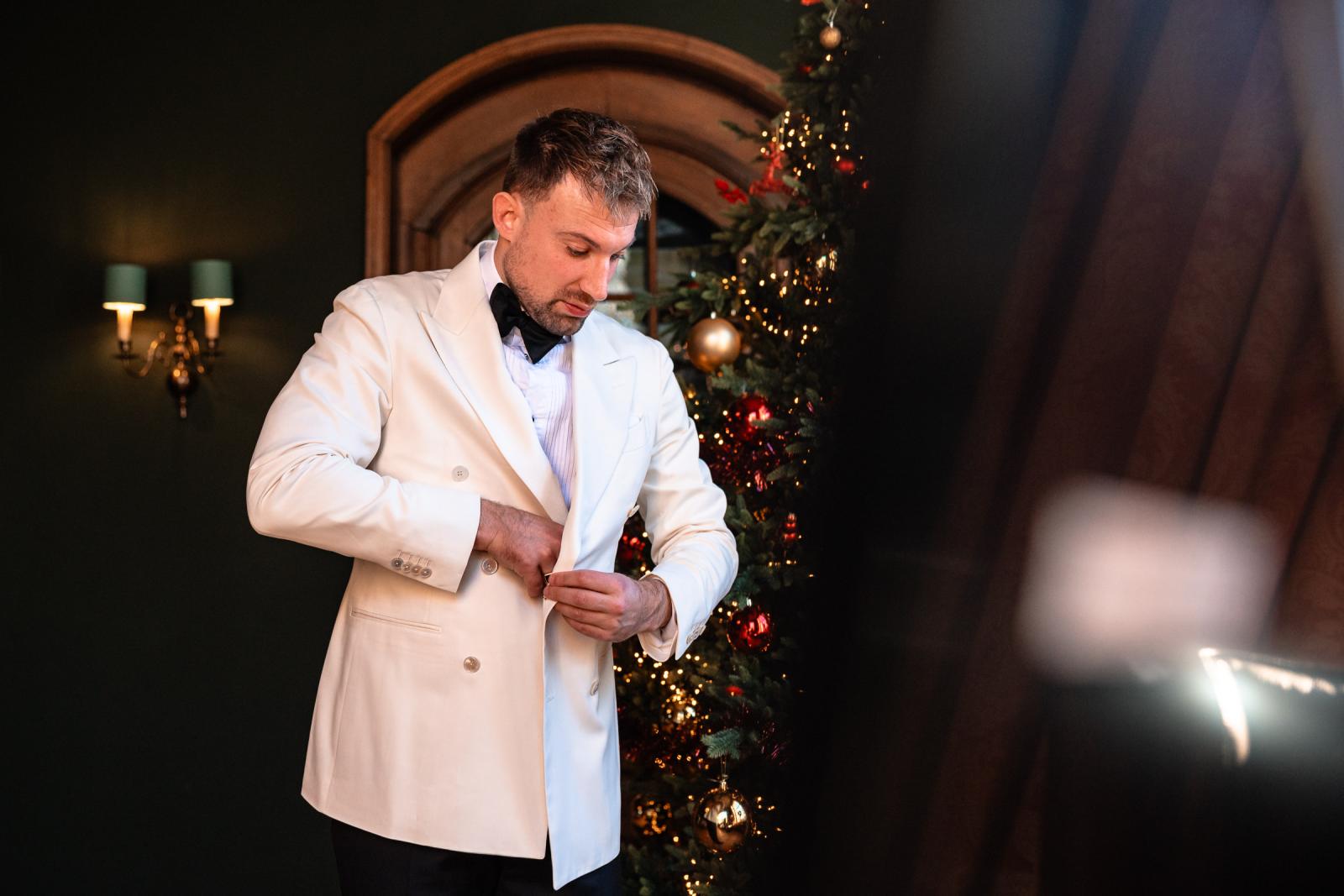 Bruidegom knoopt zijn jasje dicht bij de kerstboom in het kasteel.