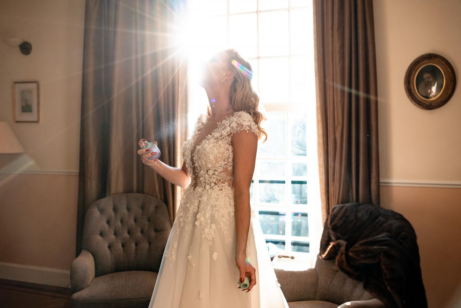 Bruid sprayt parfum met zonlicht door het raam, kerstbruiloft sfeer.