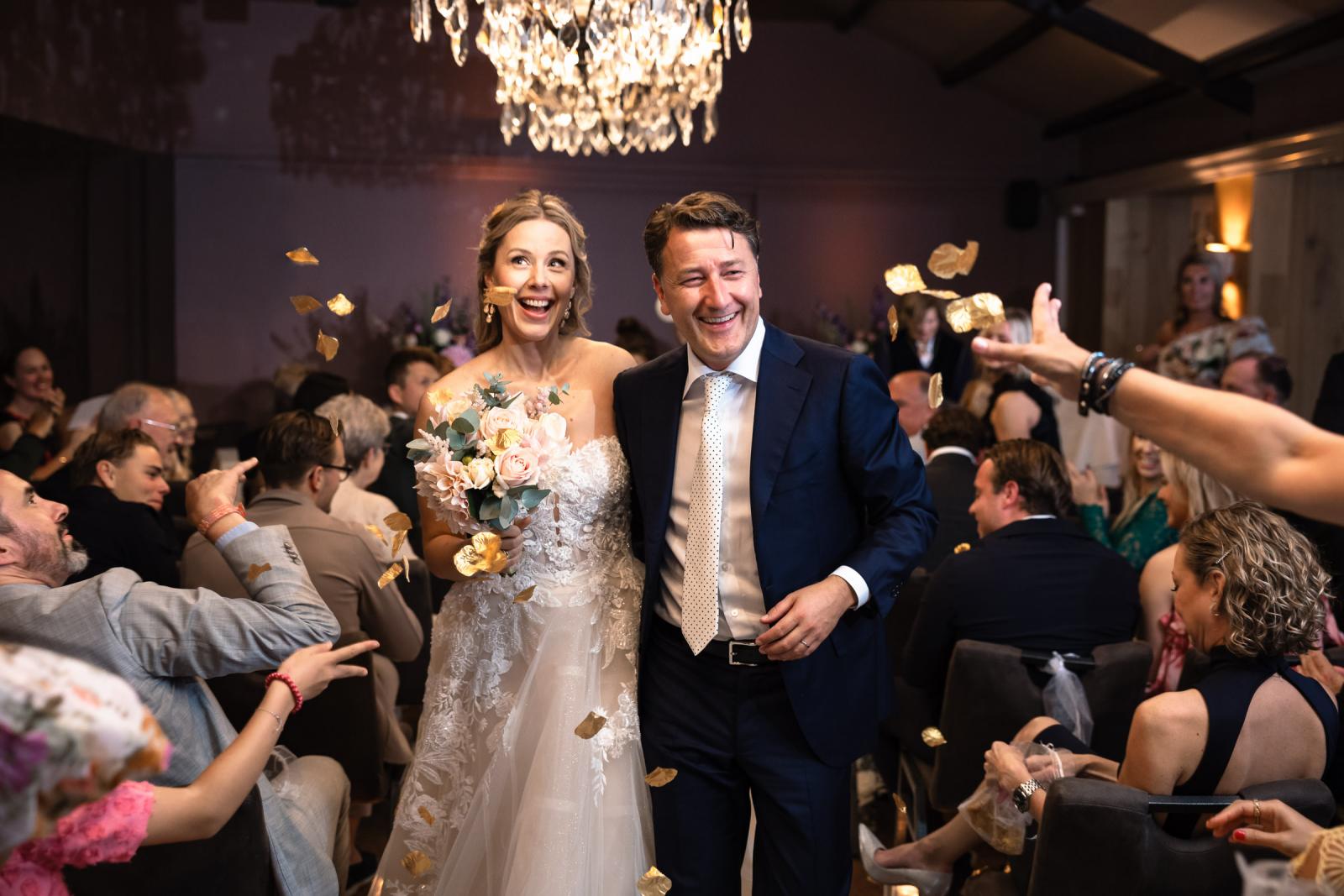 Bruidspaar loopt blij onder gegooide bloemblaadje weg na de ceremonie bij Villa Beukenhof