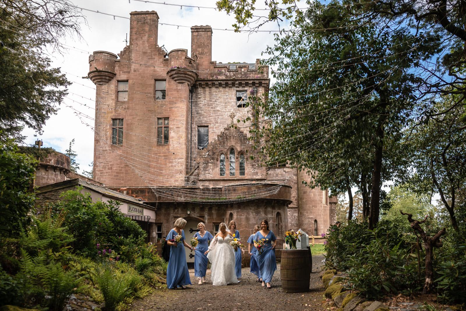 Bride Emma walking down a gravel path outside Culdees Castle Estate with her bridesmaids holding vibrant wild flower wedding bouquets.