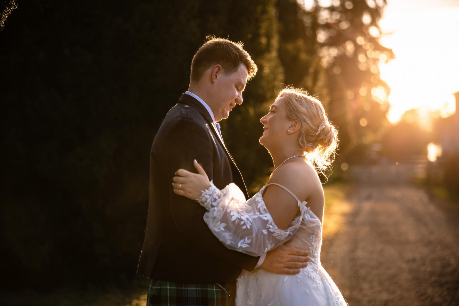 An intimate, close-up sunset portrait of Emma and Hamish embracing and smiling warmly at each other as the golden sunlight catches the bride's hair.