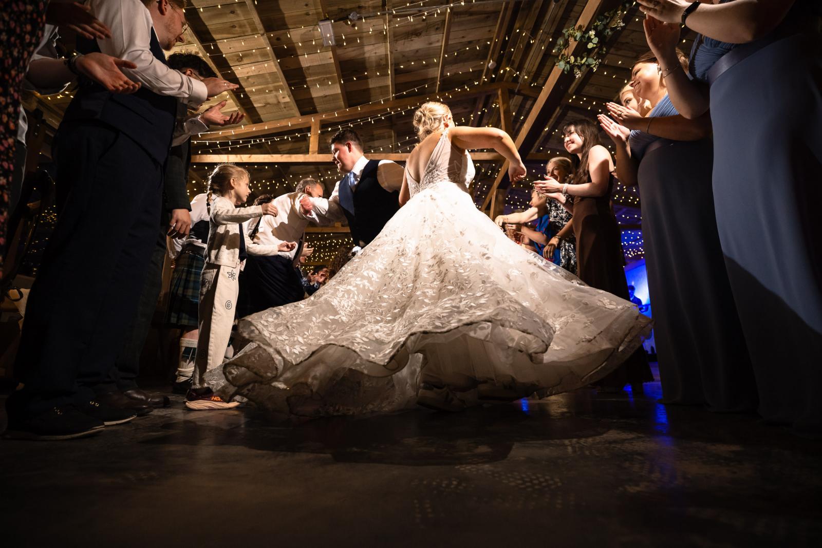 Low-angle shot capturing the motion of bride Emma's beautiful lace wedding gown as she twirls dynamically during a traditional Ceilidh dance.