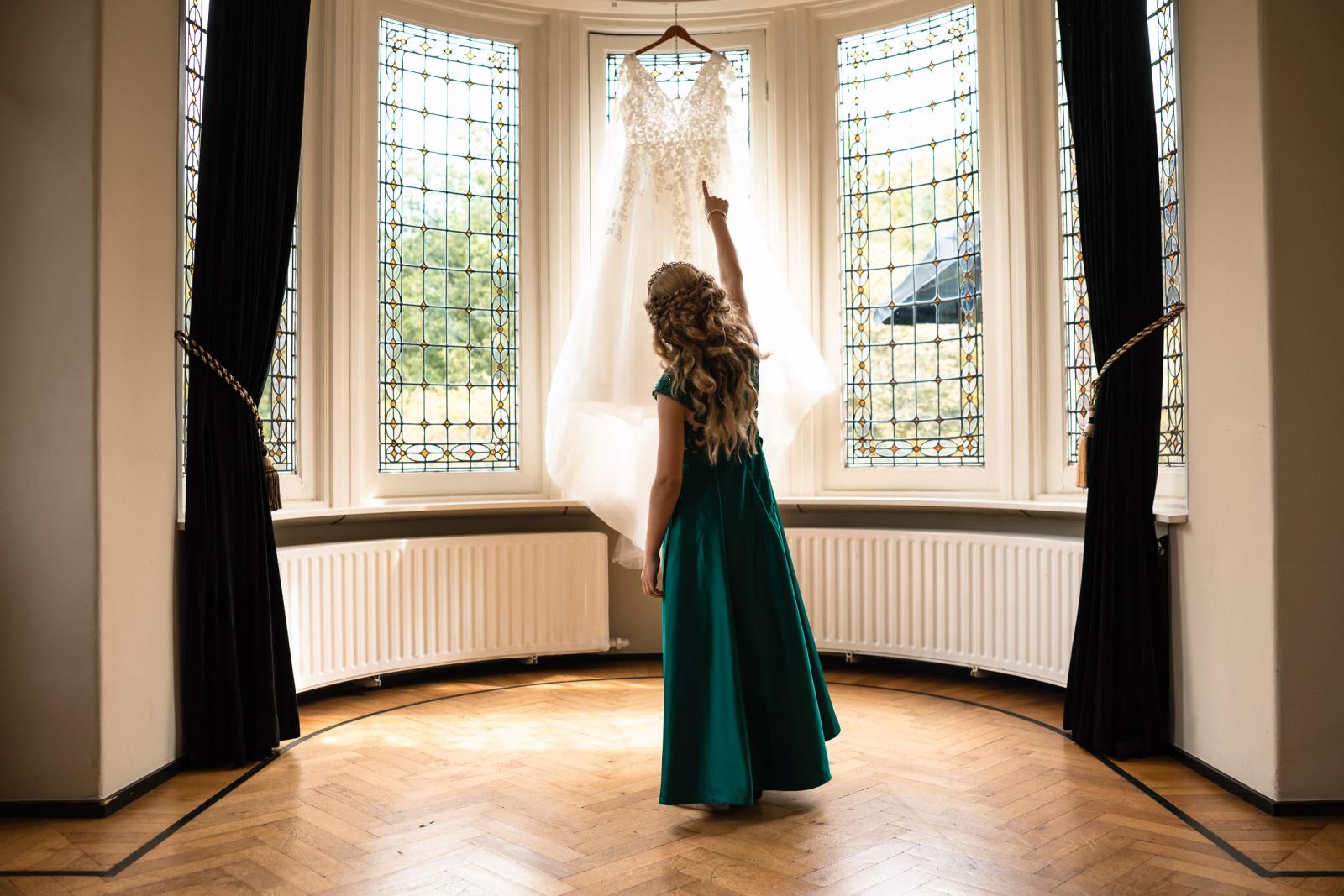 Een jong meisje bewondert de trouwjurk van de bruid in een statige kamer van Kasteel De Hooge Vuursche.