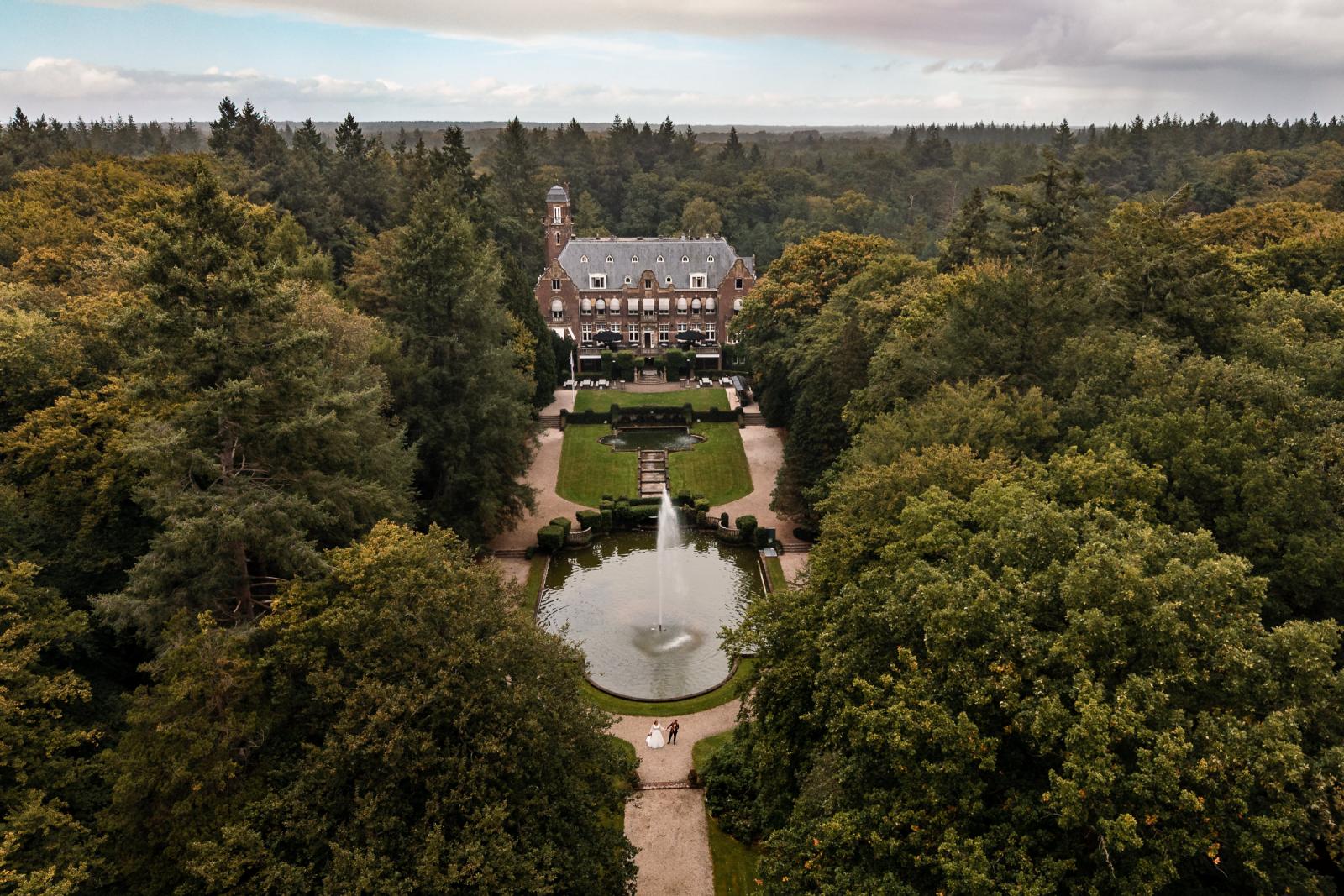 Dronefoto van Kasteel De Hooge Vuursche in Baarn met de twee bruiden bij de fontein in de kasteeltuin.