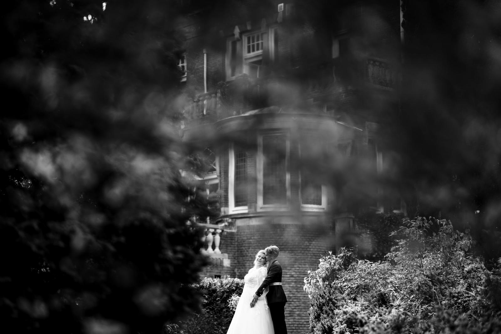 Romantisch zwart-wit portret van de twee bruiden voor het kasteel, gefotografeerd tussen het groen.
