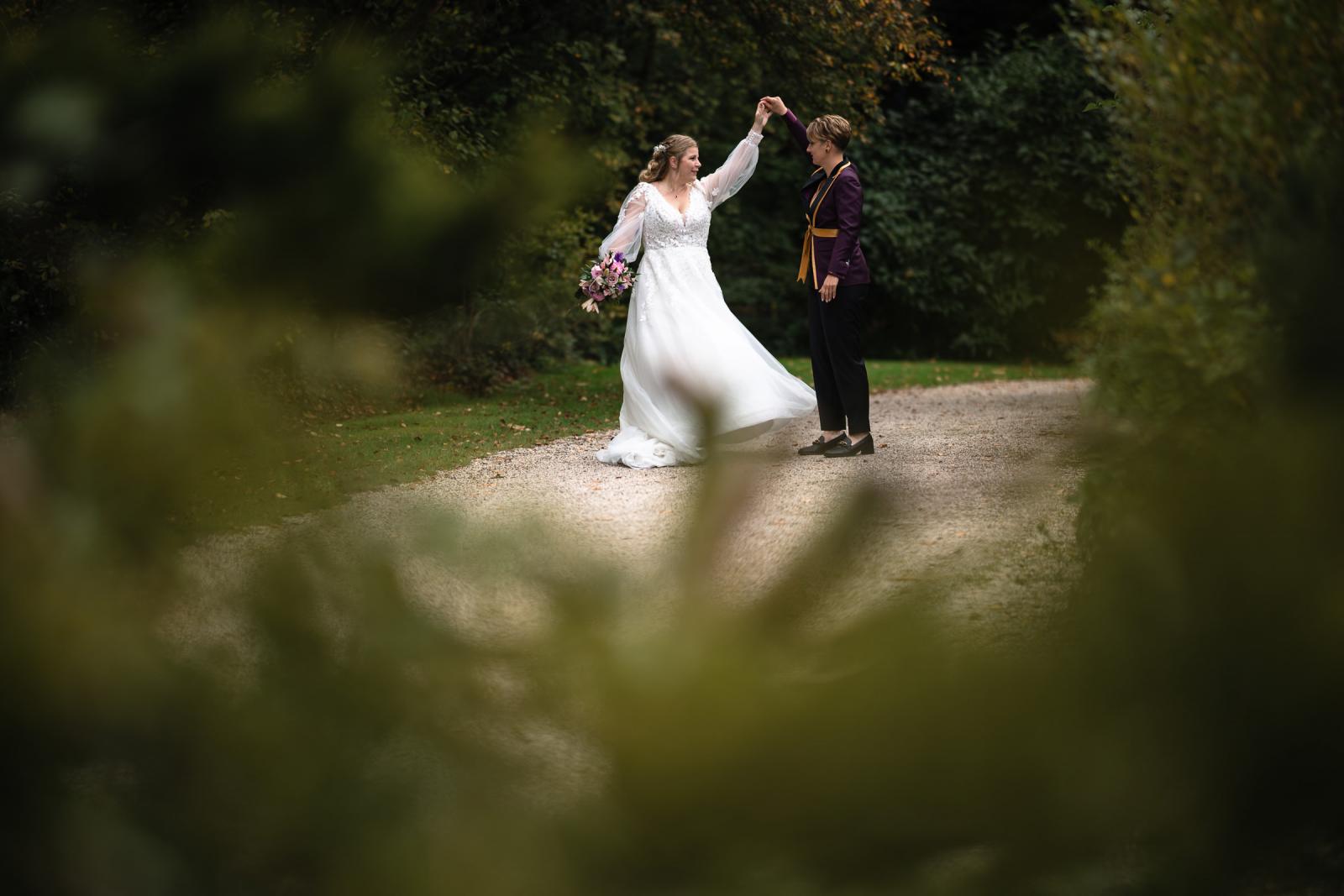 De twee bruiden dansen samen op het grindpad van Kasteel De Hooge Vuursche, omringd door herfstkleuren.