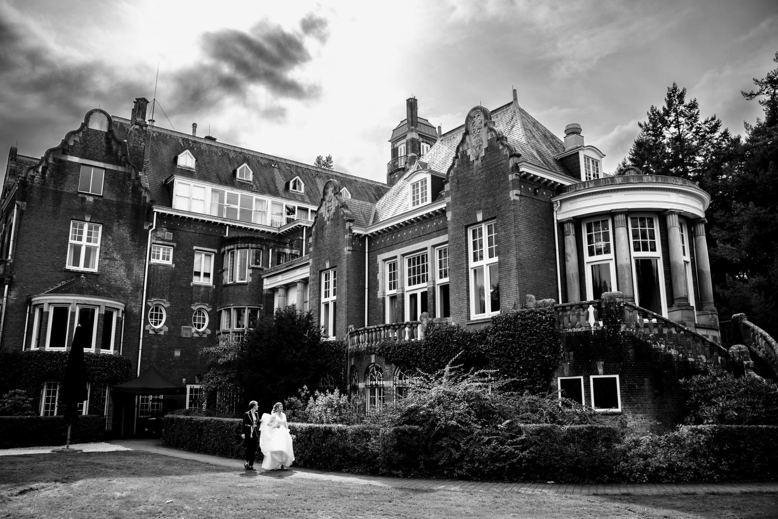 Zwart-wit overzicht van het kasteel met de twee bruiden die samen wandelen over het grasveld.