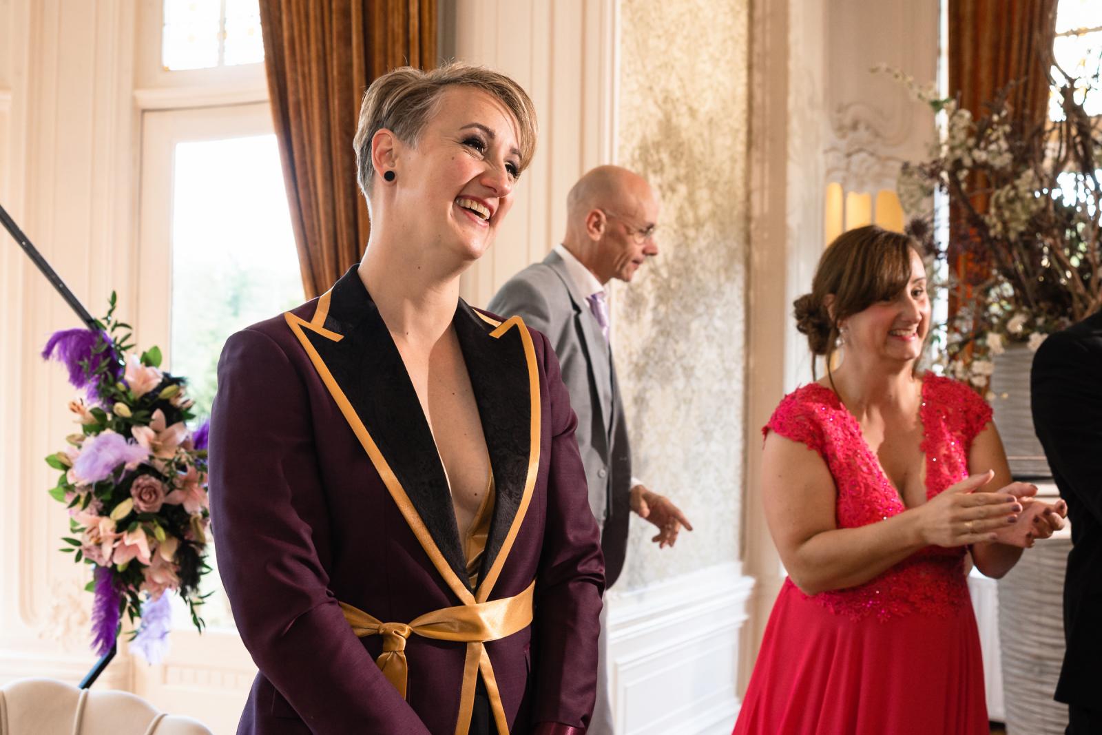 De tweede bruid kijkt ontroerd toe bij het binnenkomen van haar partner, omringd door familie en vrienden.