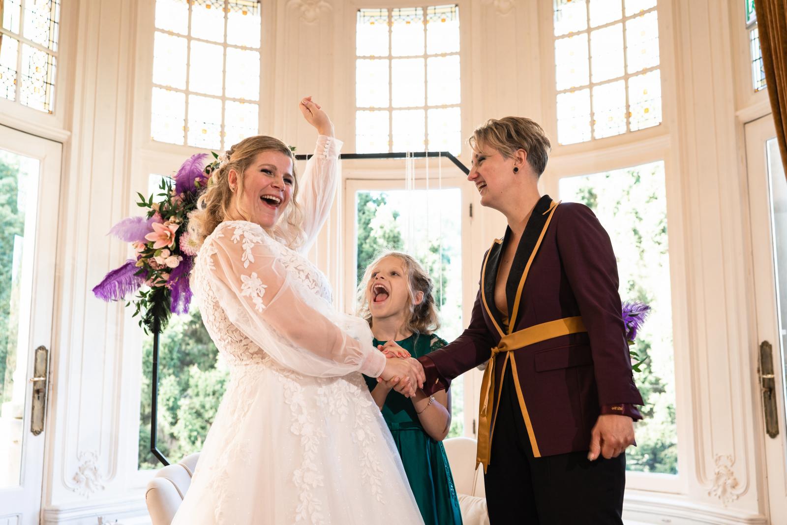 De bruiden vieren hun jawoord met opgeheven handen terwijl hun dochter enthousiast tussen hen in staat.