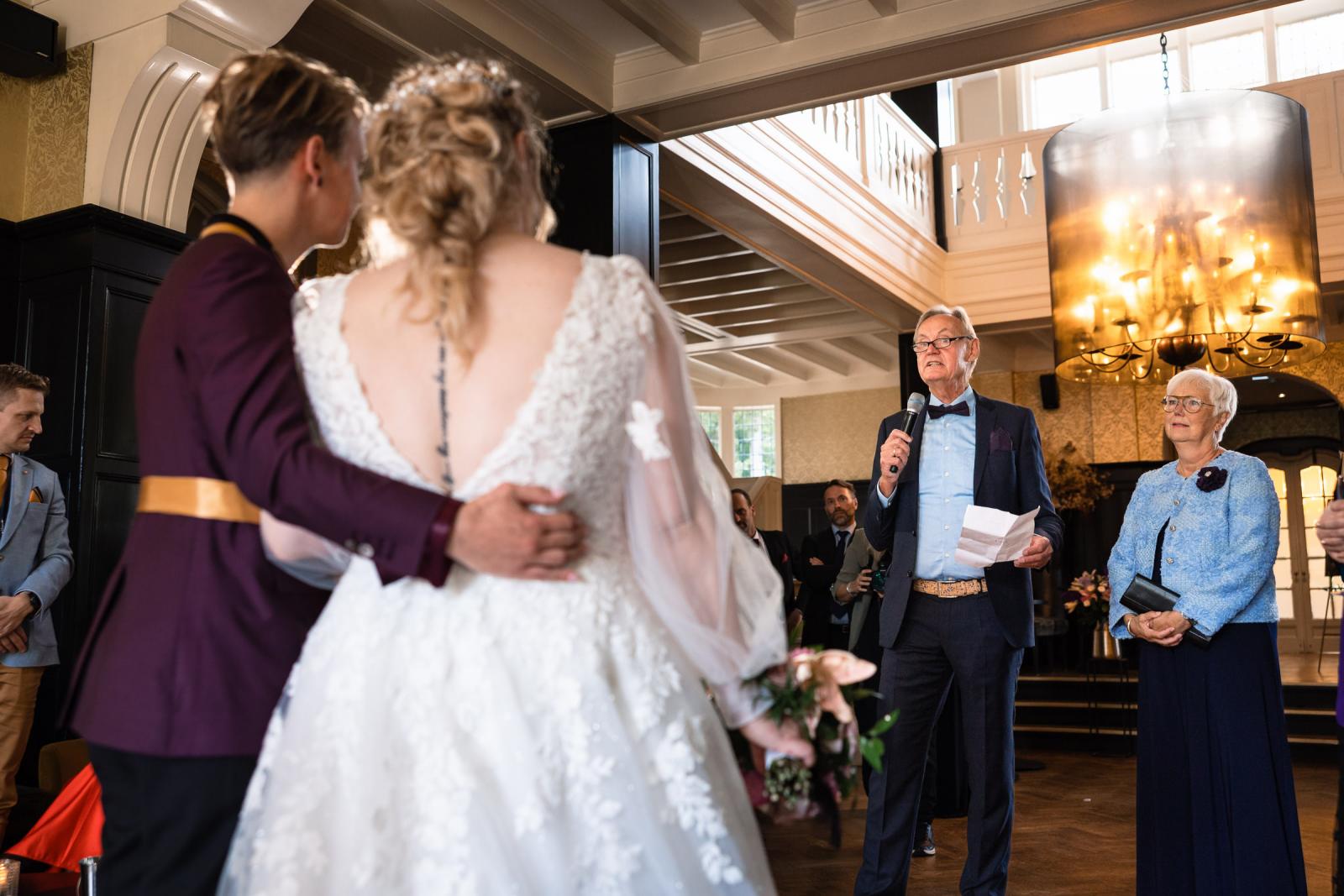 Een vader houdt een emotionele speech tijdens de borrel terwijl de twee bruiden luisteren.