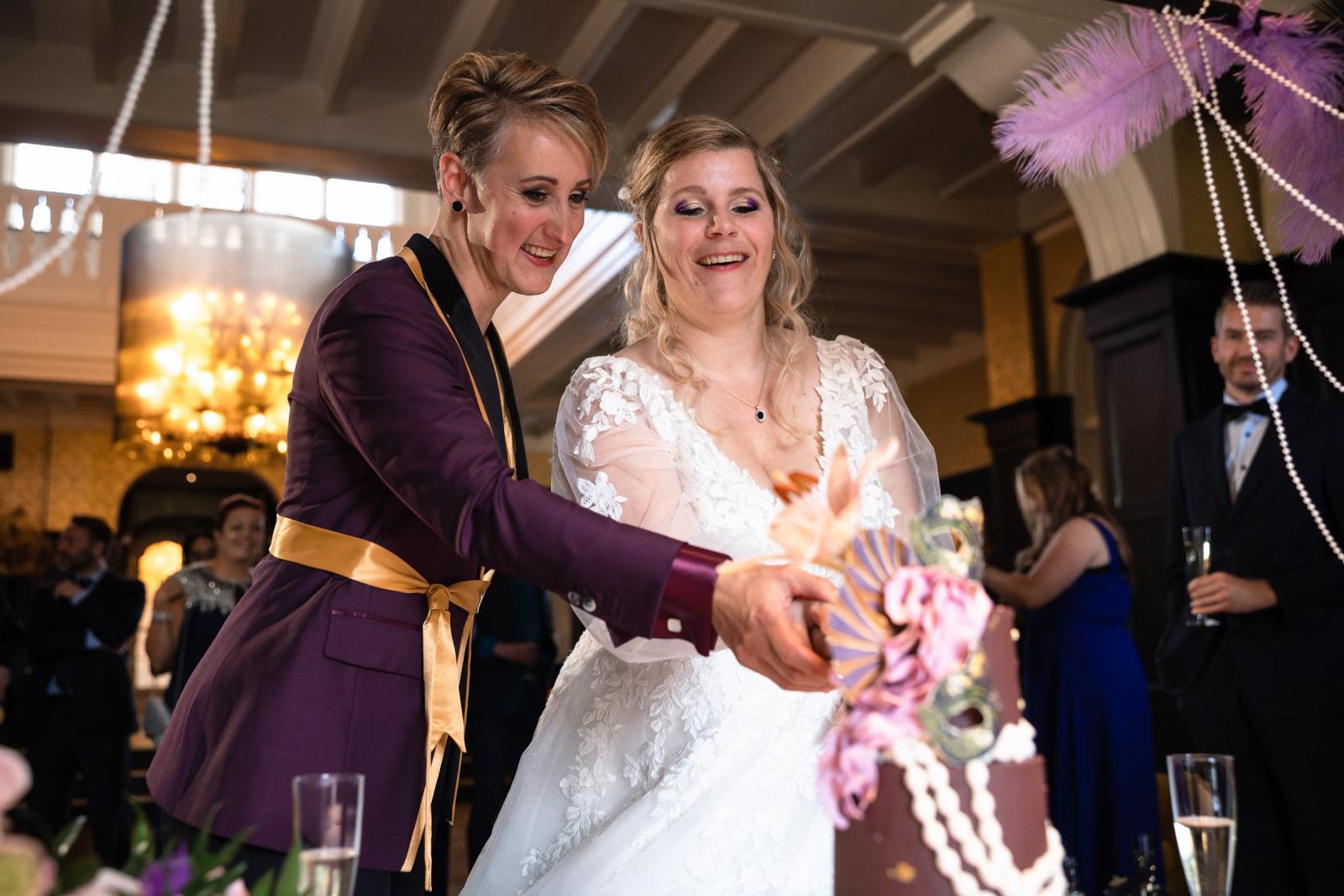 De twee bruiden snijden samen de bruidstaart aan, omringd door familie en vrienden.