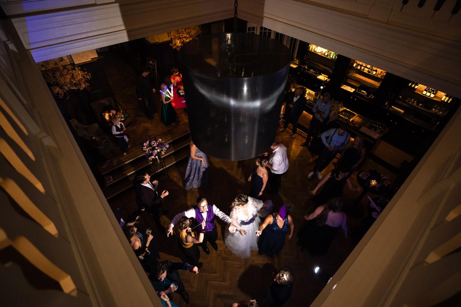 Overzicht van de feestzaal van bovenaf, waar gasten dansen en genieten van de muziek.