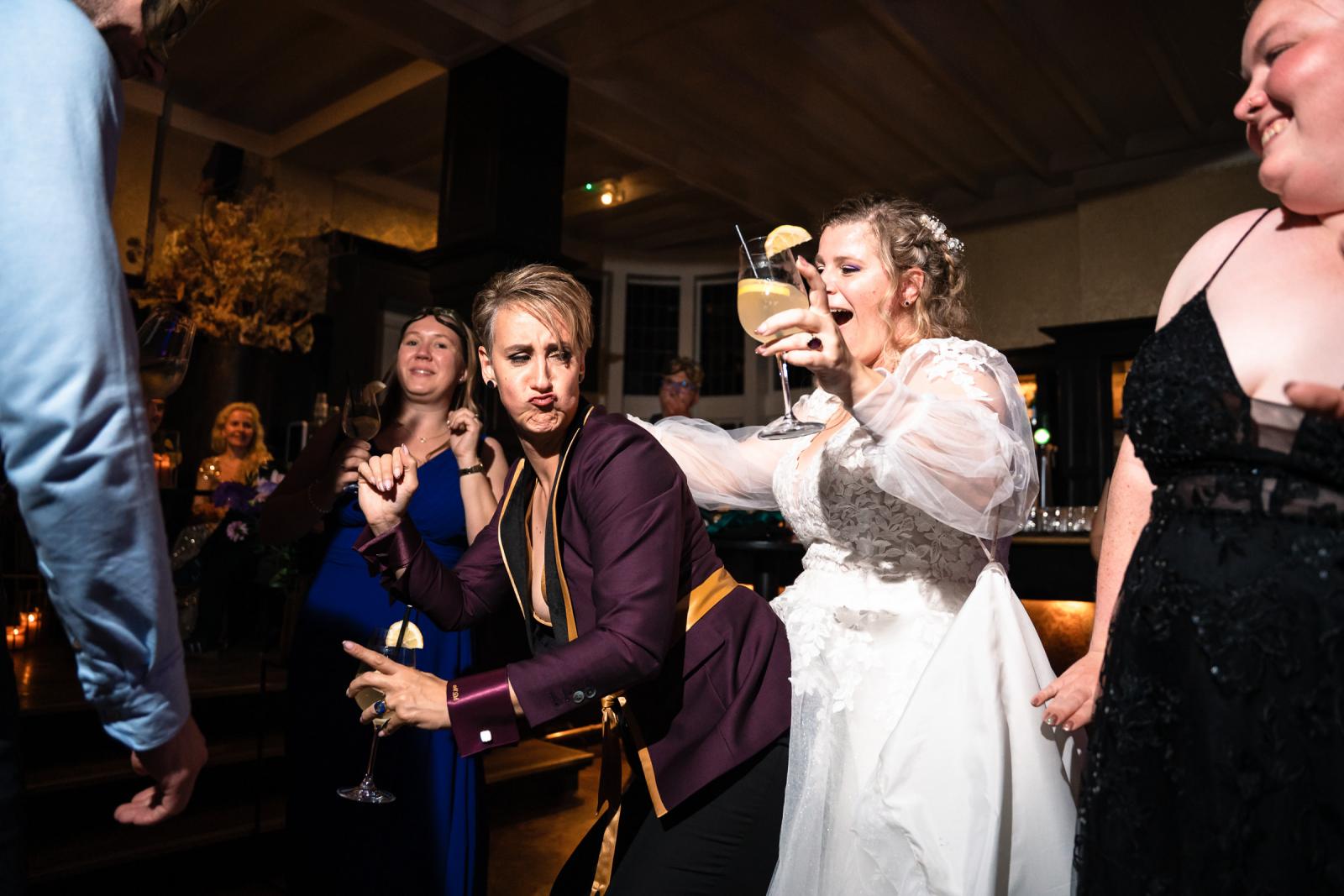 De bruiden dansen samen met vrienden tijdens het avondfeest, met een cocktail in de hand.