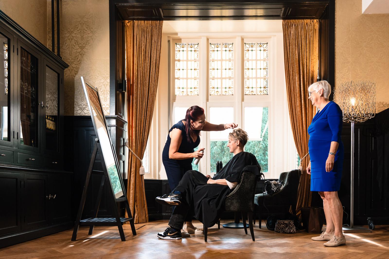 De visagiste brengt de make-up aan bij een van de bruiden terwijl haar moeder toekijkt.