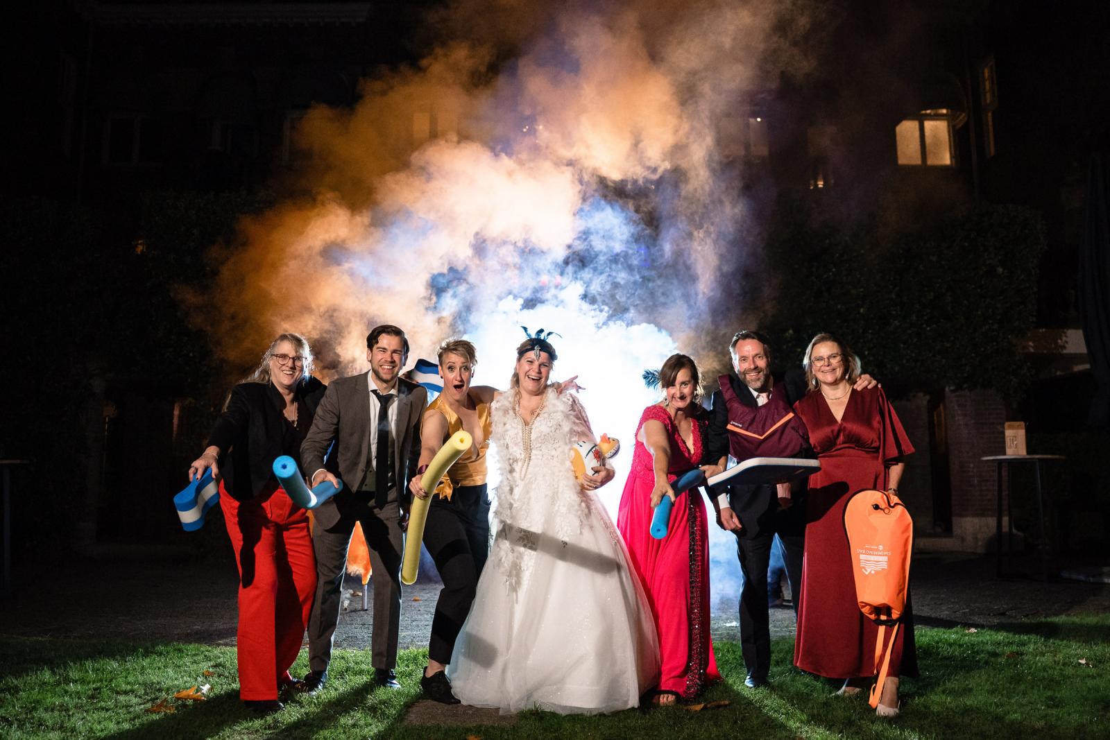 De bruiden poseren met vrienden en familie voor een rookshow met felgekleurde nevel in de tuin van Kasteel De Hooge Vuursche.