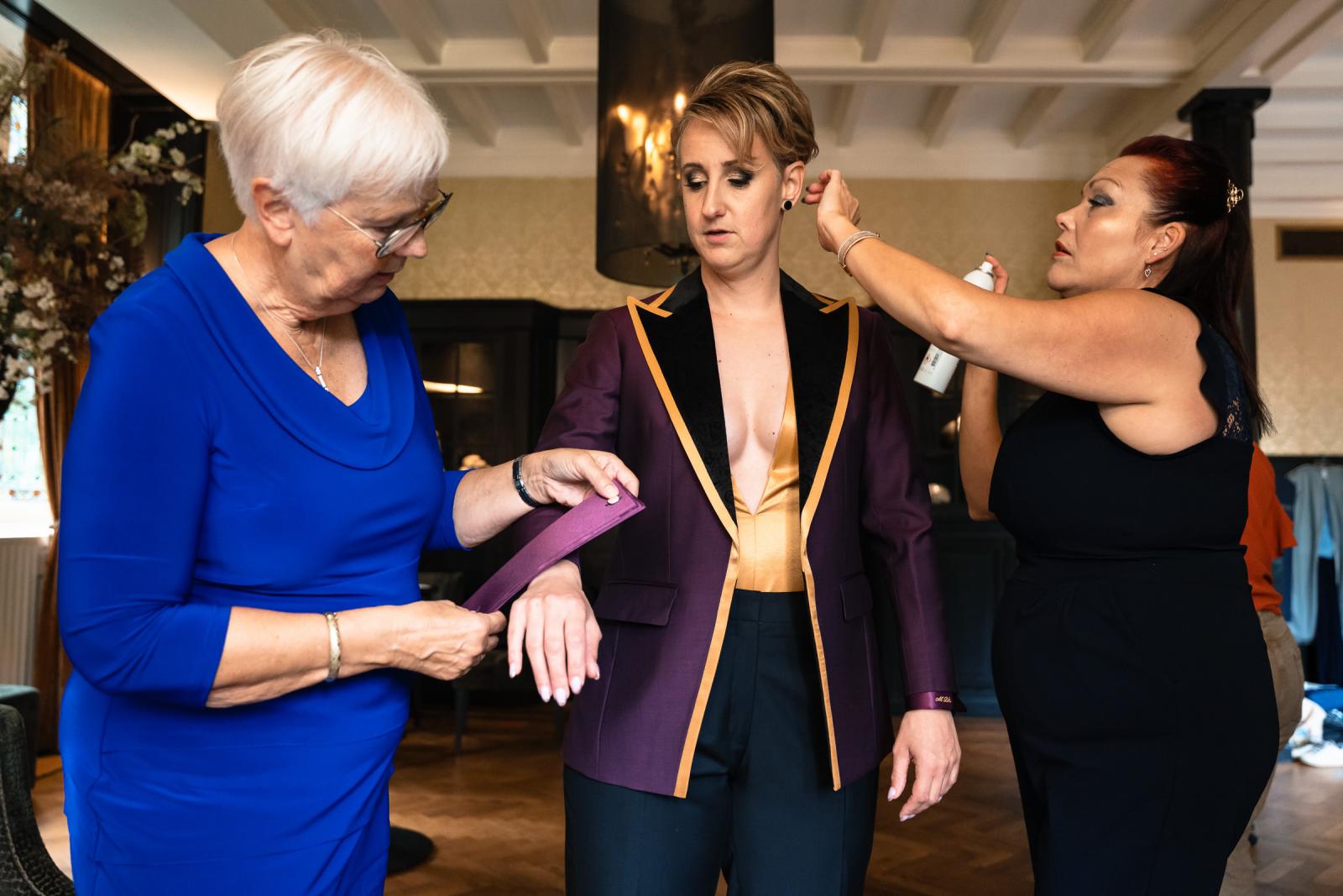 De andere bruid trekt haar paarse trouwpak aan met hulp van haar moeder en vriendin.