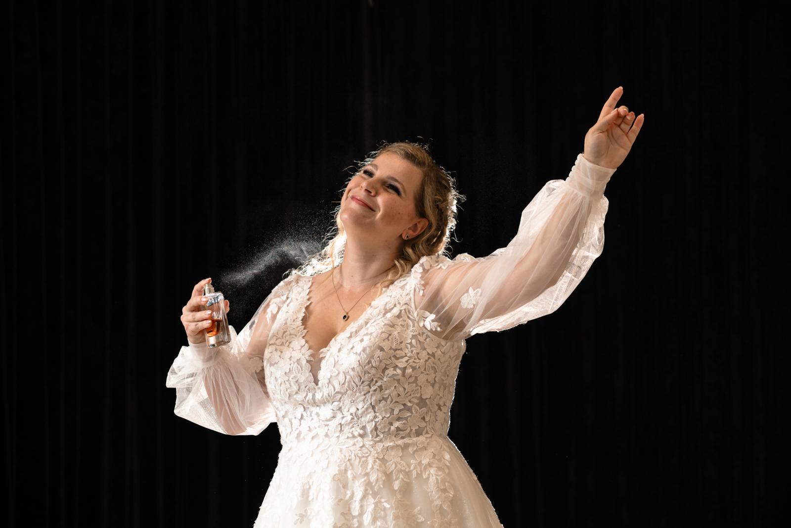 De bruid sprayt haar parfum op in haar trouwjurk, verlicht door zacht licht in het kasteel.