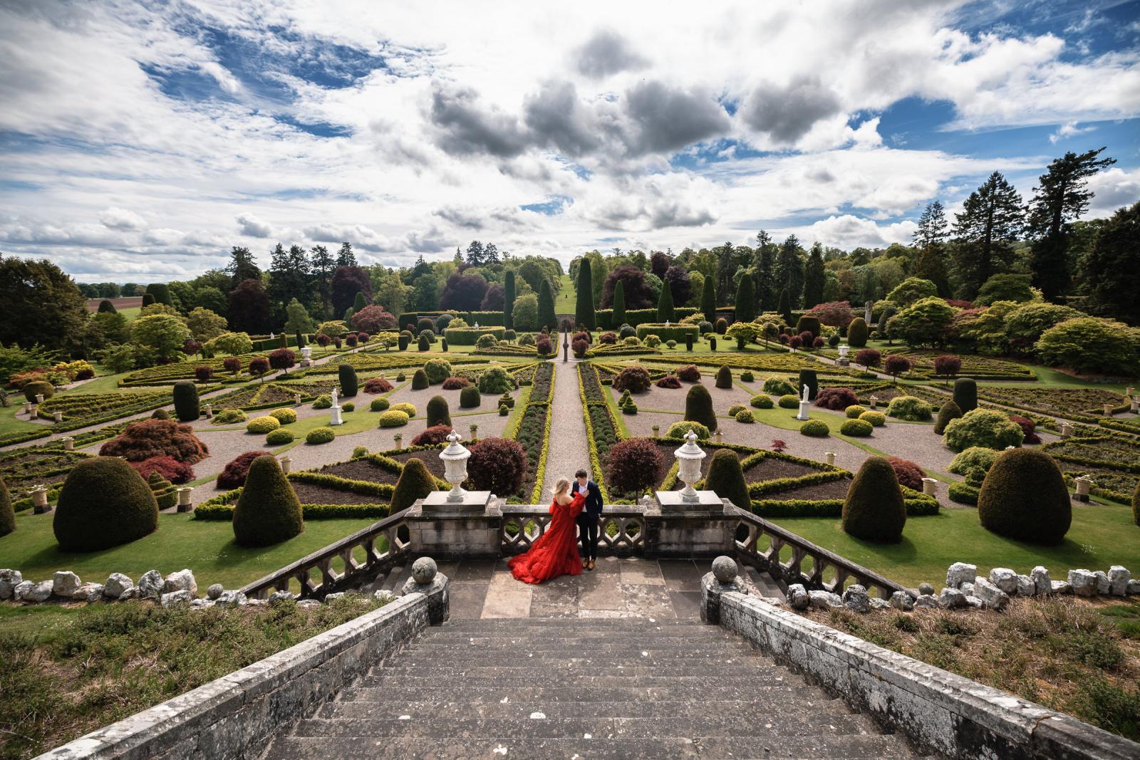 Stunning symmetrical overview of Drummond Castle Gardens featuring a couple in a red dress under an impressive cloudy sky