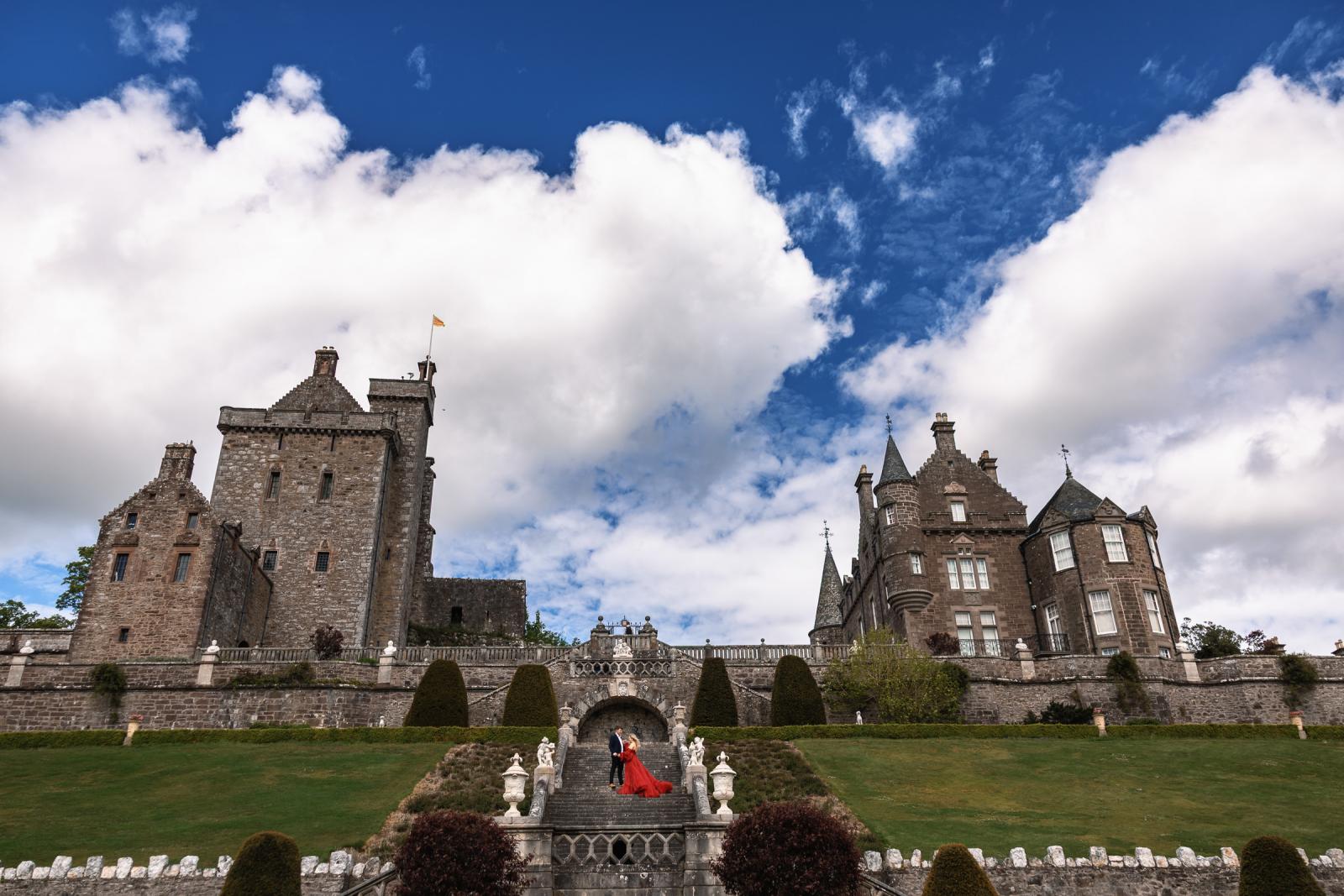 Couple posing halfway up the monumental stone kasteeltrap with Drummond Castle in the background