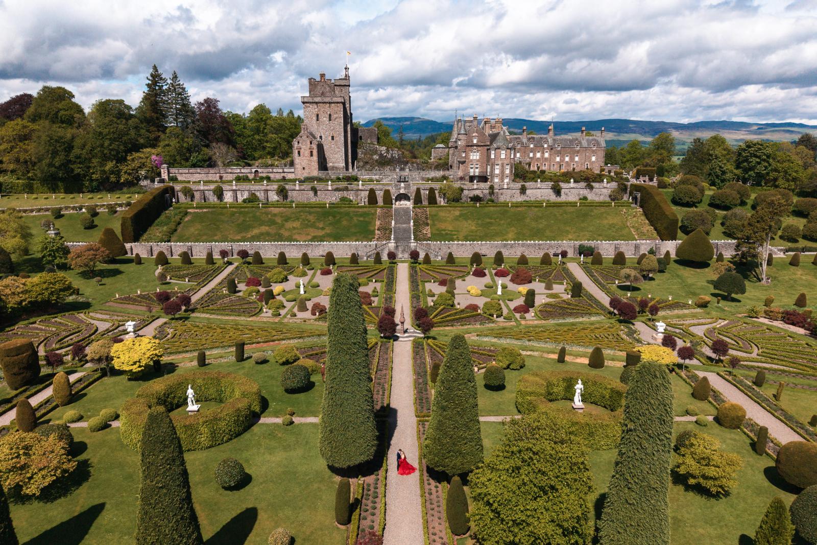 Aerial drone photography of the symmetrical gardens of Drummond Castle with the engaged couple on the central path