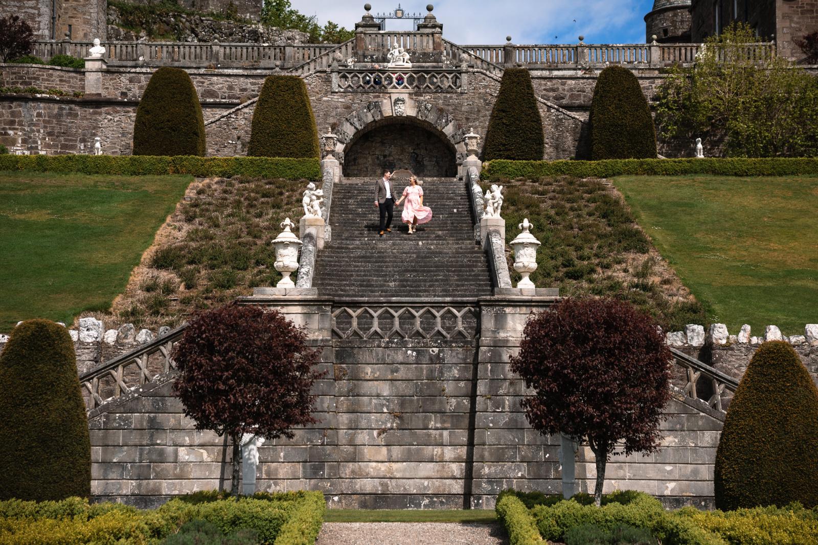 Engaged couple walking hand in hand down the historic castle stairs during a romantic Scotland engagement session