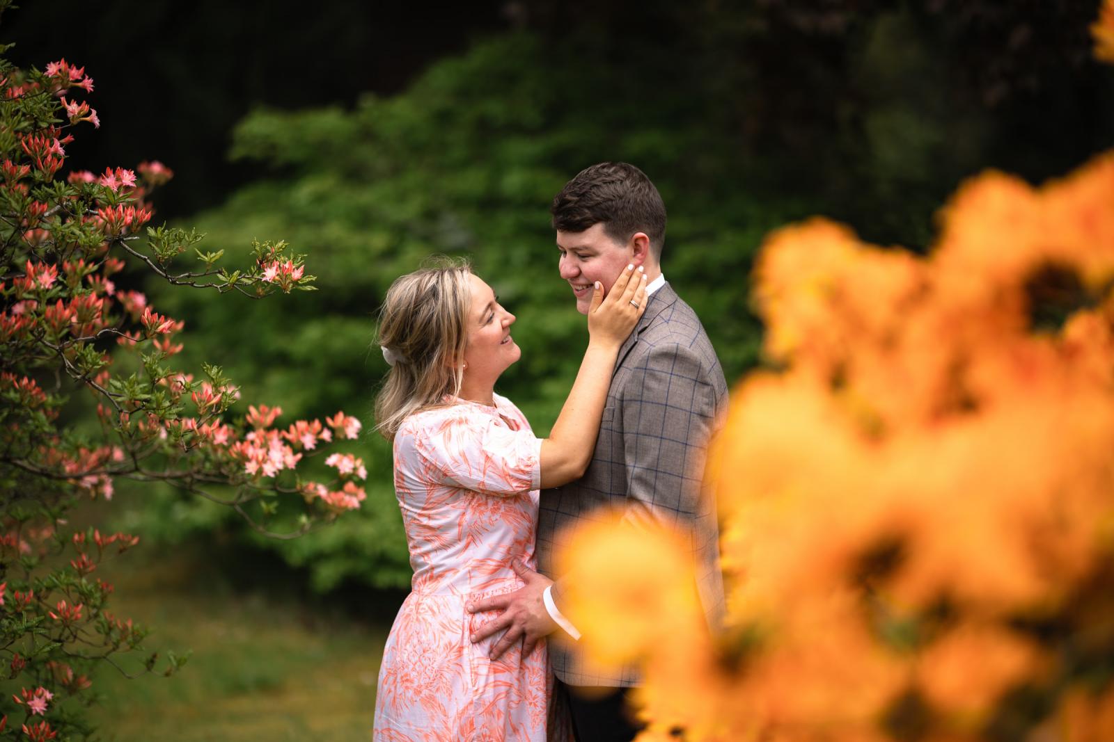 Intimate lifestyle portrait of an engaged couple surrounded by blooming orange and pink flowers in Scotland