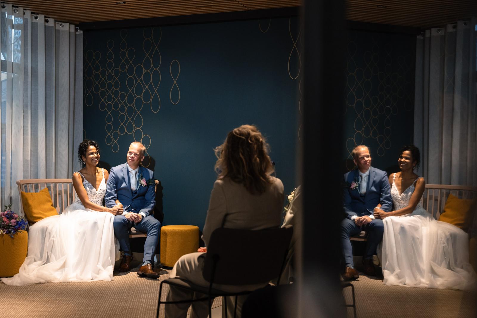 Het bruidspaar zit stralend naast elkaar tijdens de ceremonie in De Binding Heerhugowaard.