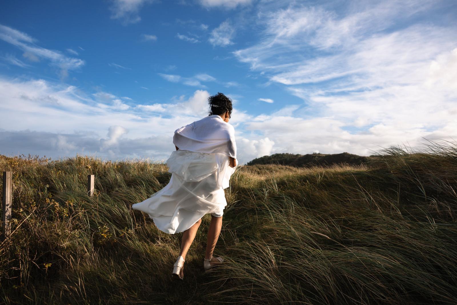 Bruid loopt door de duinen met haar jurk opgetild tijdens de herfstige bruidsreportage.